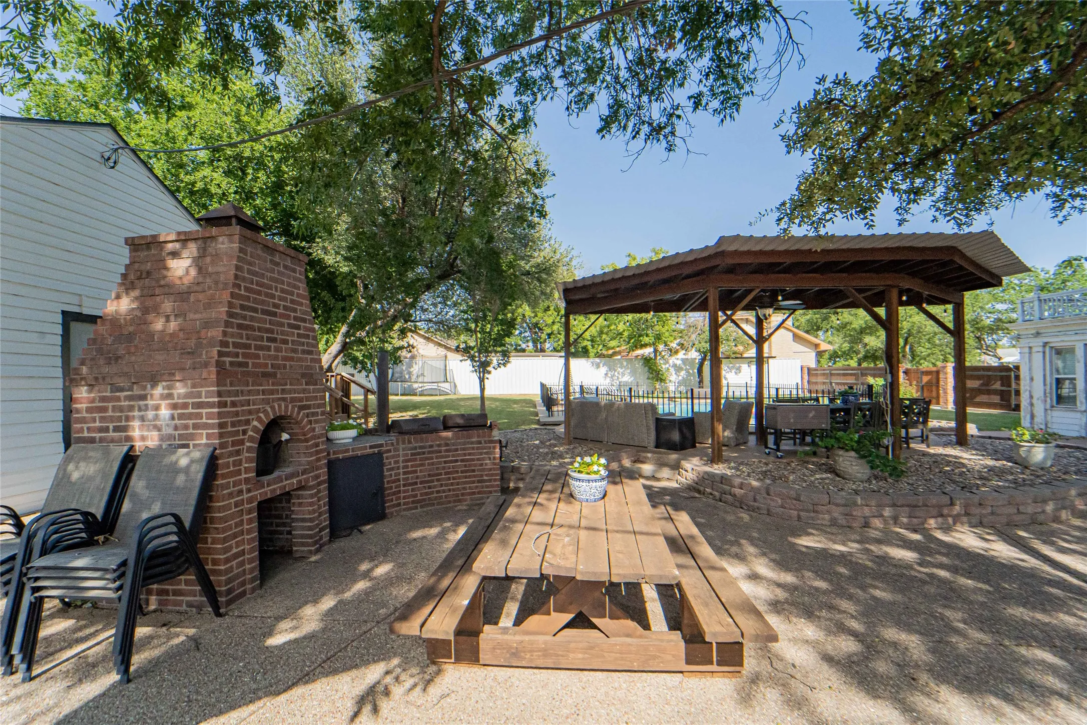 Backyard entertaining area featuring a built-in brick oven, a spacious wood gazebo with a metal roof, and a gravel-paved patio