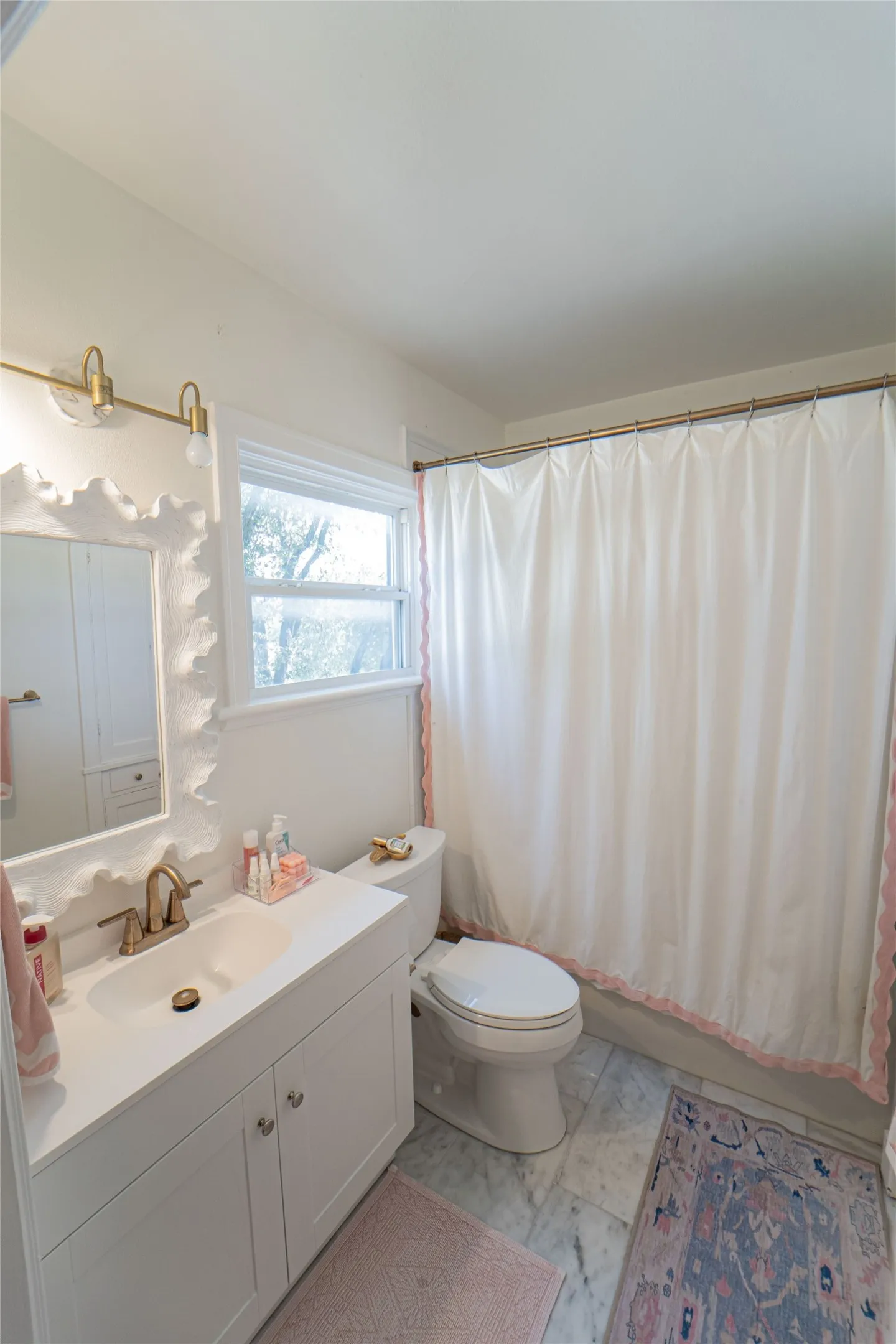 Bathroom featuring a white vanity with integrated sink, brass-finish faucet, and a window above the toilet