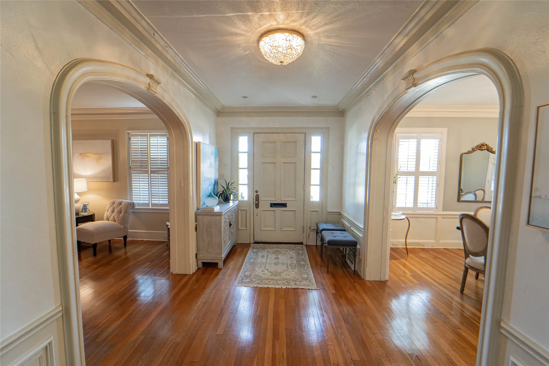 Entry foyer featuring polished wood flooring, detailed archways, a paneled front door with side lights, and a decorative ceiling light fixture