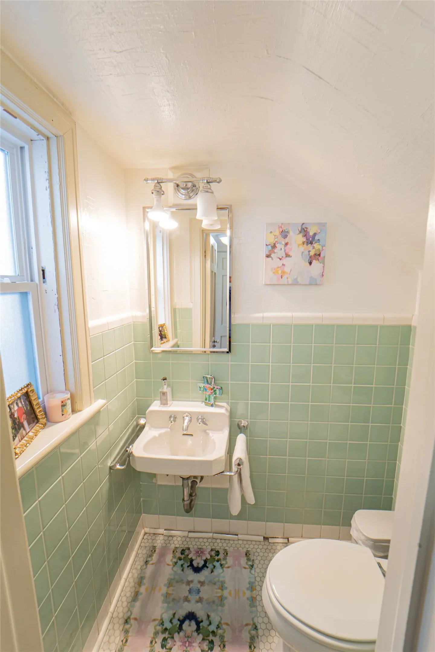 Bathroom featuring light green square wall tiles, a white wall-mounted basin, a chrome-framed mirror, and a white toilet