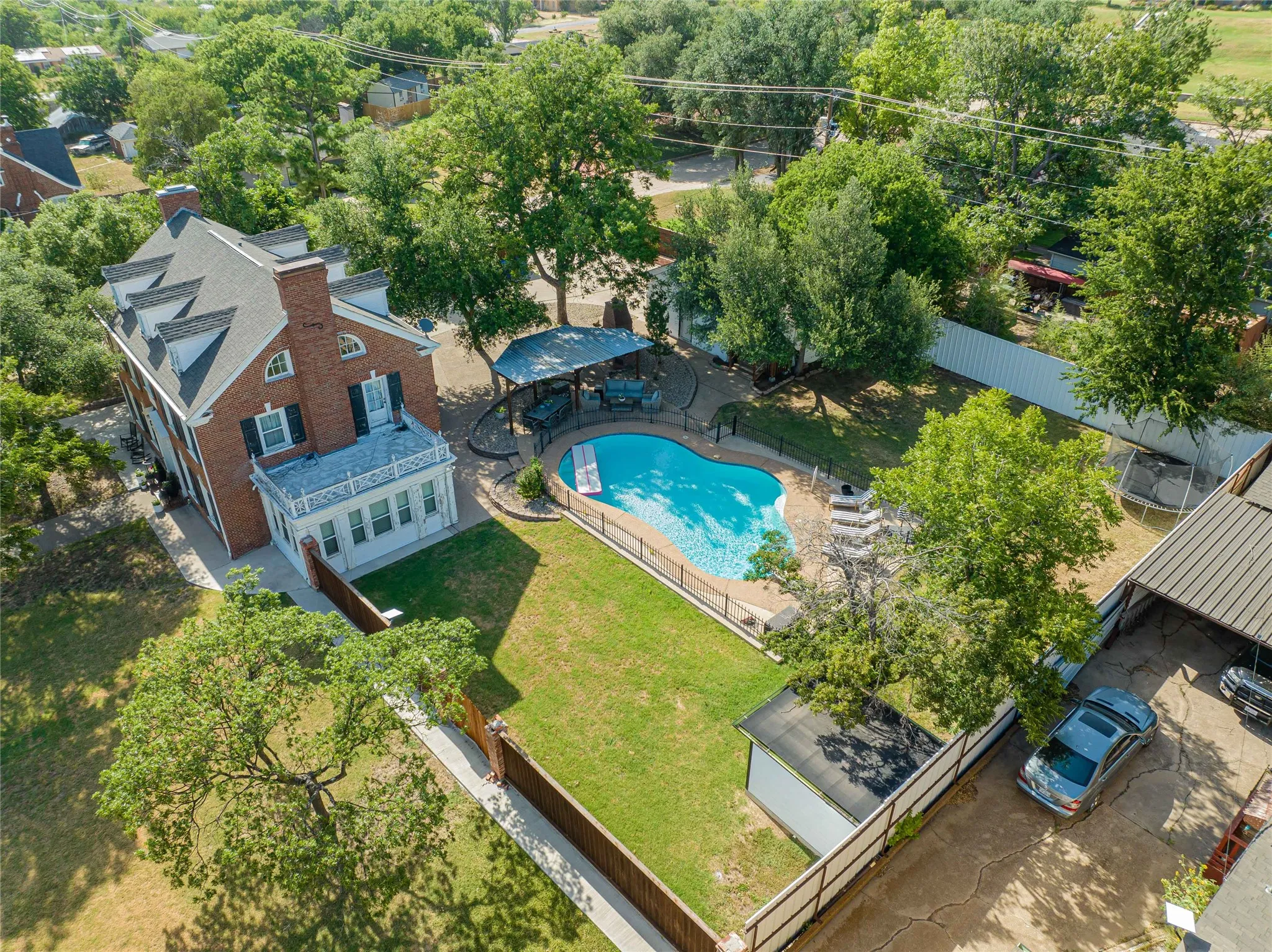 Brick exterior colonial residence featuring a gabled roofline with dormer windows, a second-story balcony with white railing, and a ground-level sunroom