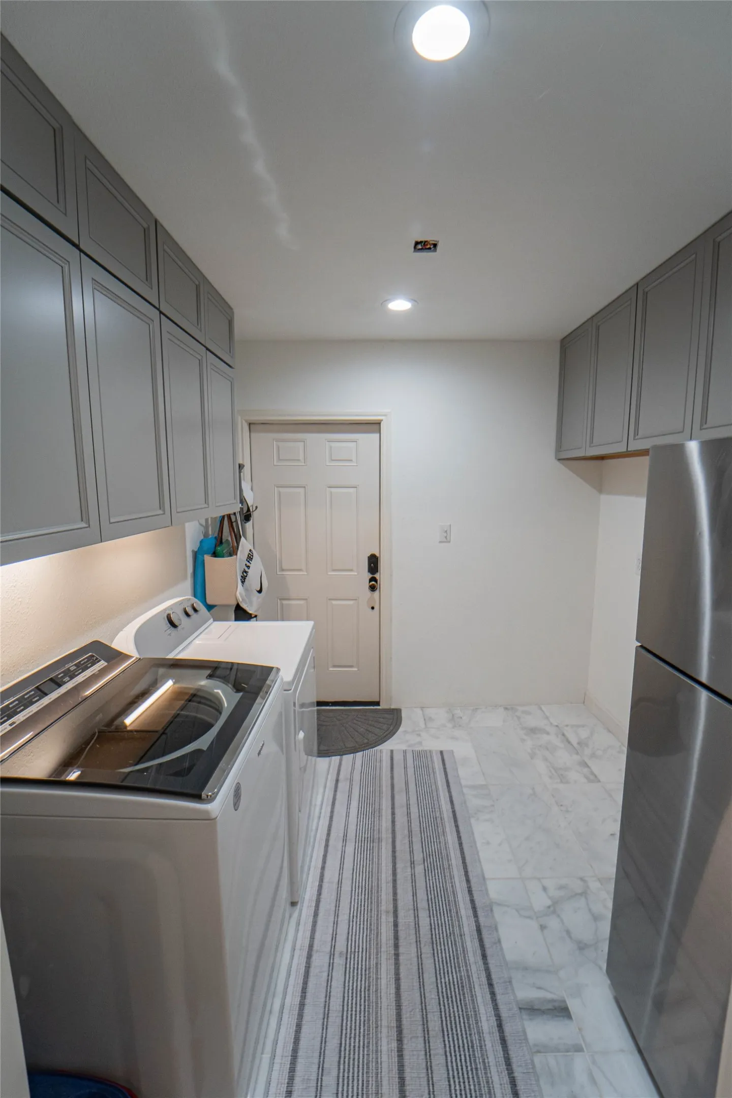 Laundry space featuring recessed lighting, white walls, gray cabinetry, and light-toned tile flooring