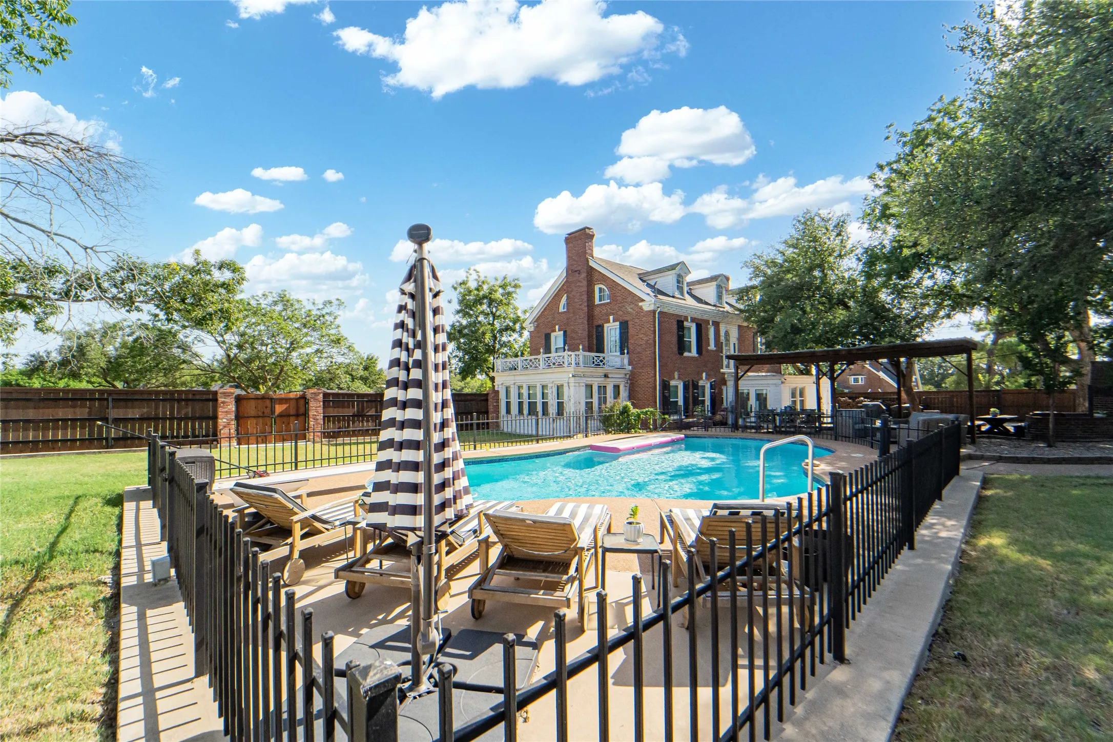 Expansive outdoor living area featuring a sparkling in-ground pool, surrounding concrete patio, and black wrought iron fencing