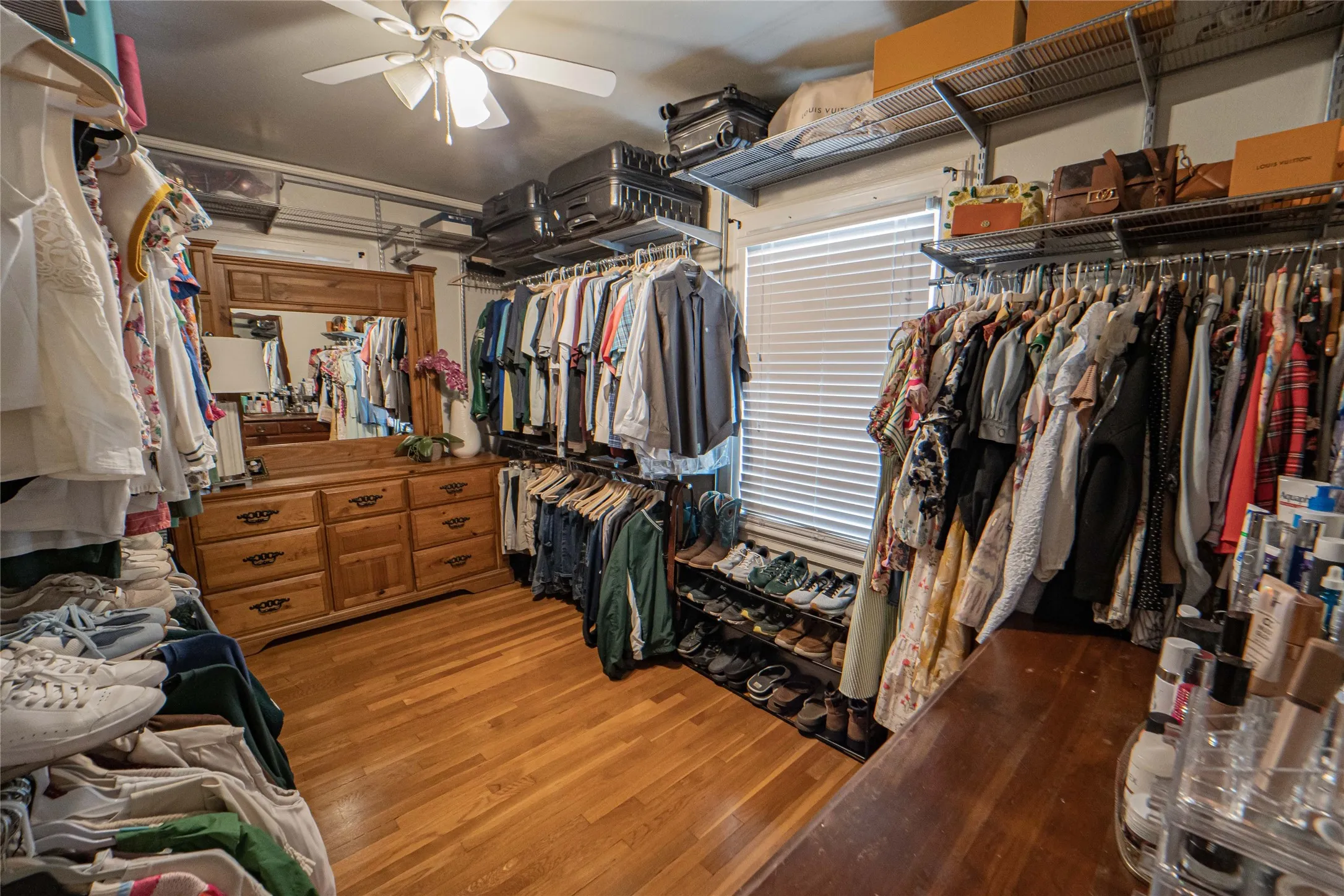 Walk-in closet featuring wood-finish flooring, a ceiling fan, a window with blinds, and extensive built-in shelving and hanging storage