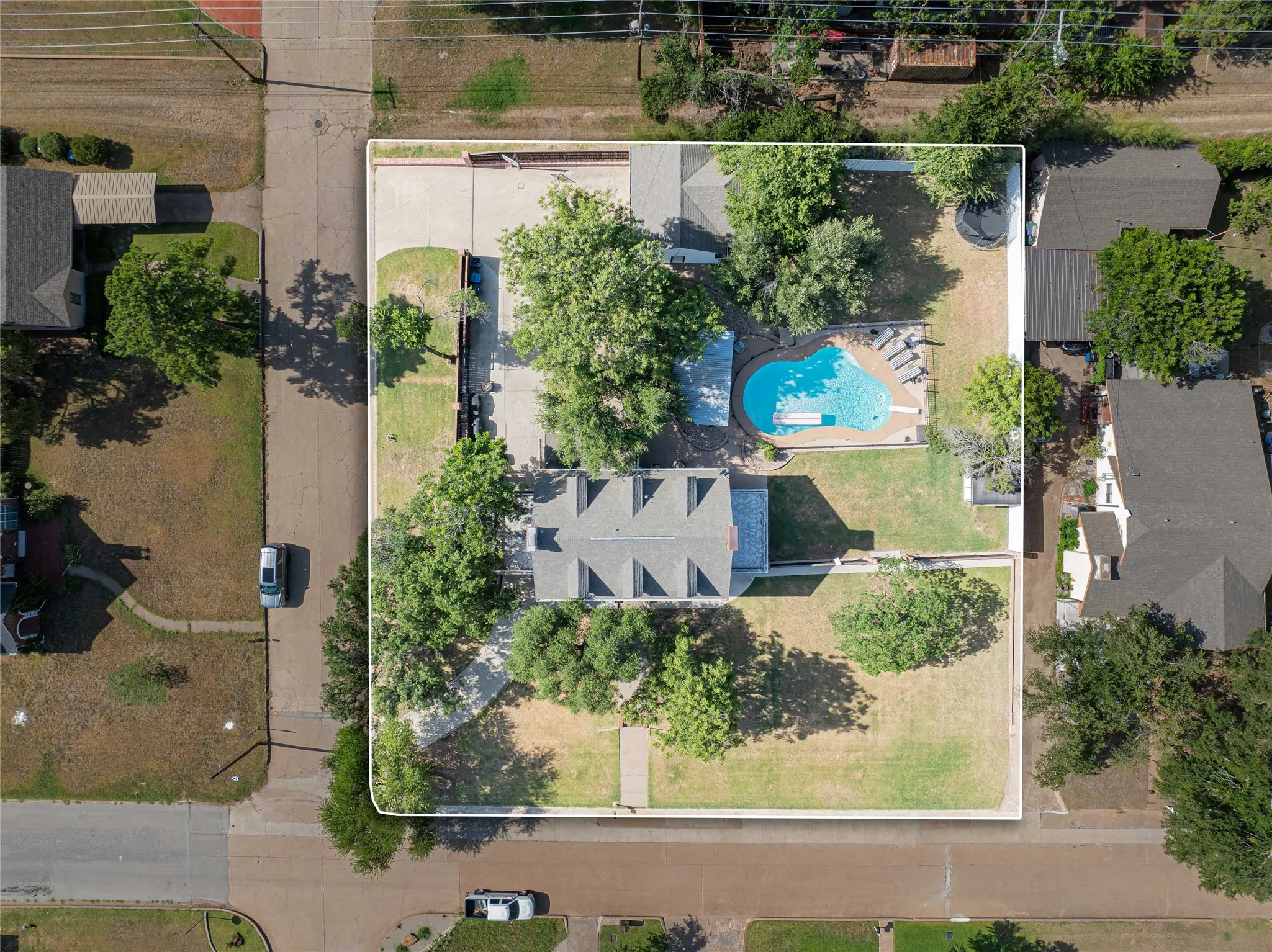 Expansive property featuring a large residence with a multi-gabled roof, a private swimming pool, mature trees, a substantial paved driveway, and a spacious grassy yard