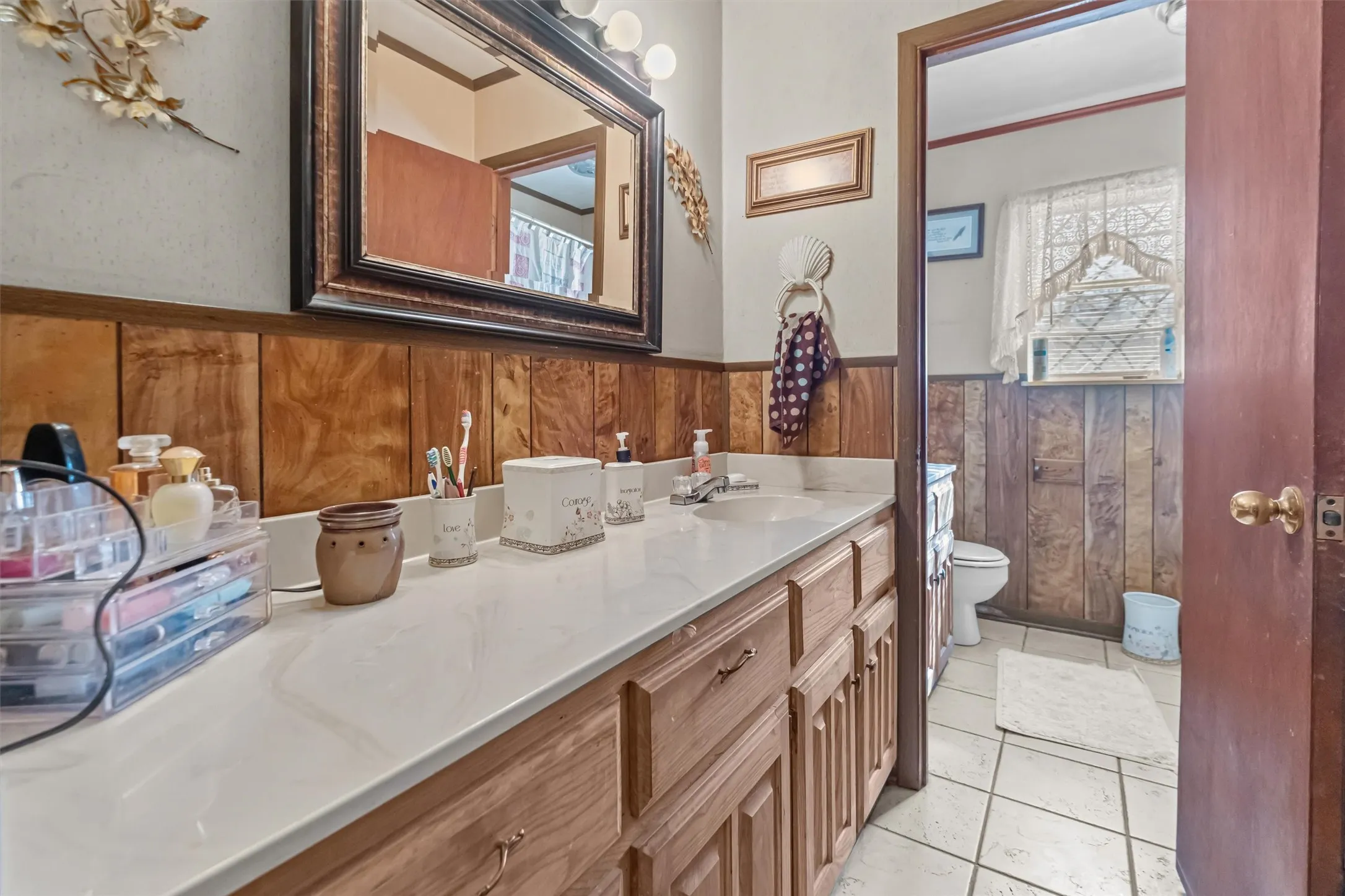 Bathroom vanity featuring a light-toned countertop, wood-finish cabinetry, and a large framed mirror with overhead vanity lighting