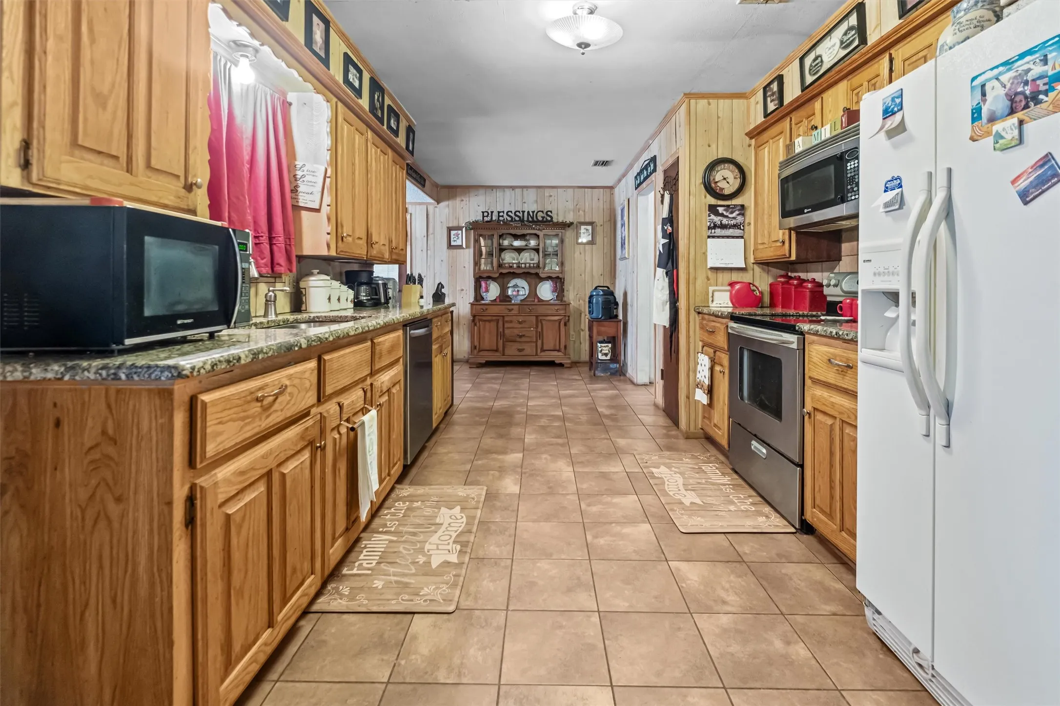 Galley kitchen featuring wood-finish cabinetry, granite-style countertops, tile flooring, and integrated appliances
