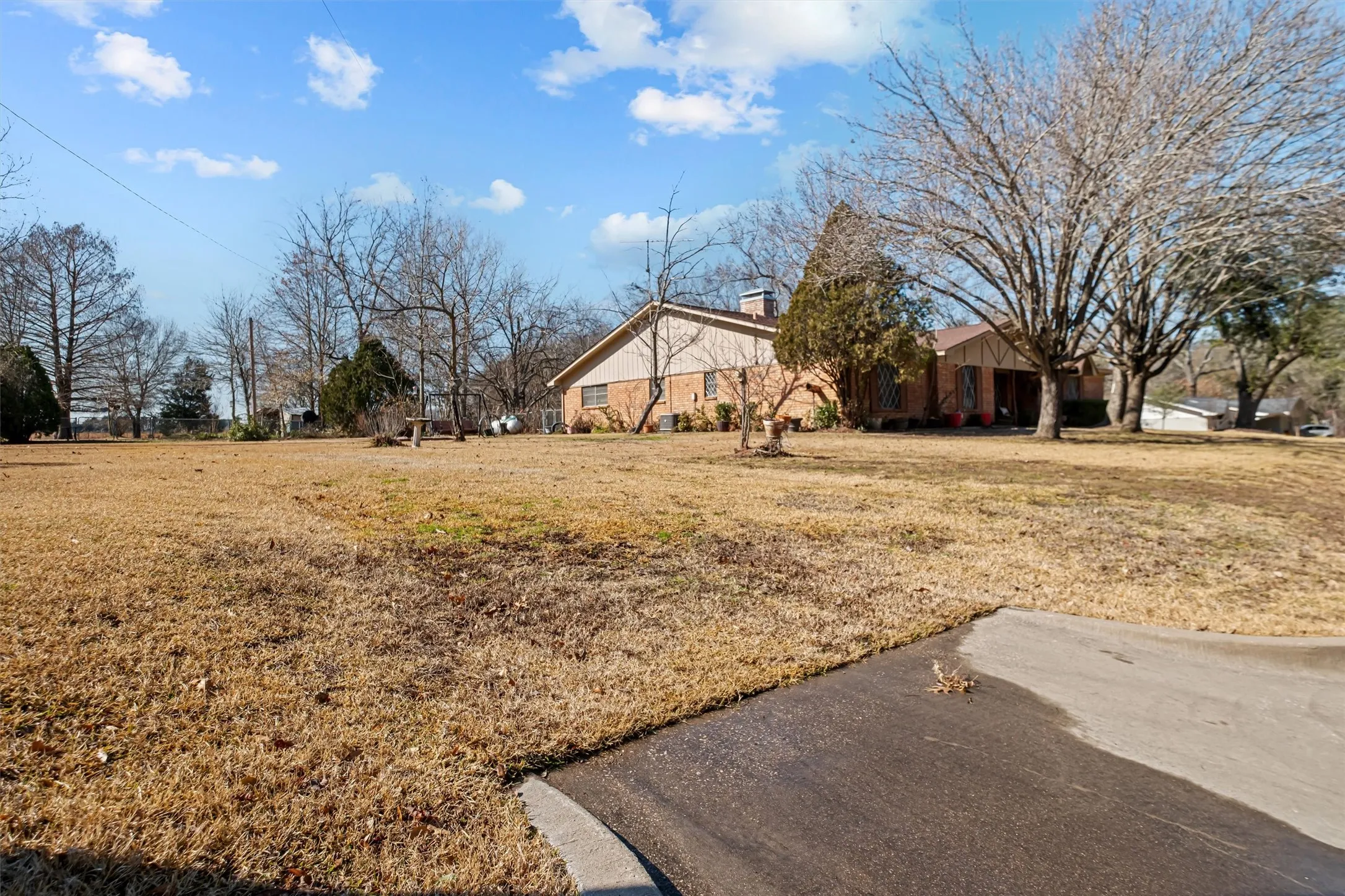 Expansive front yard featuring a paved driveway, mature trees, and a brick exterior with a light-colored soffit