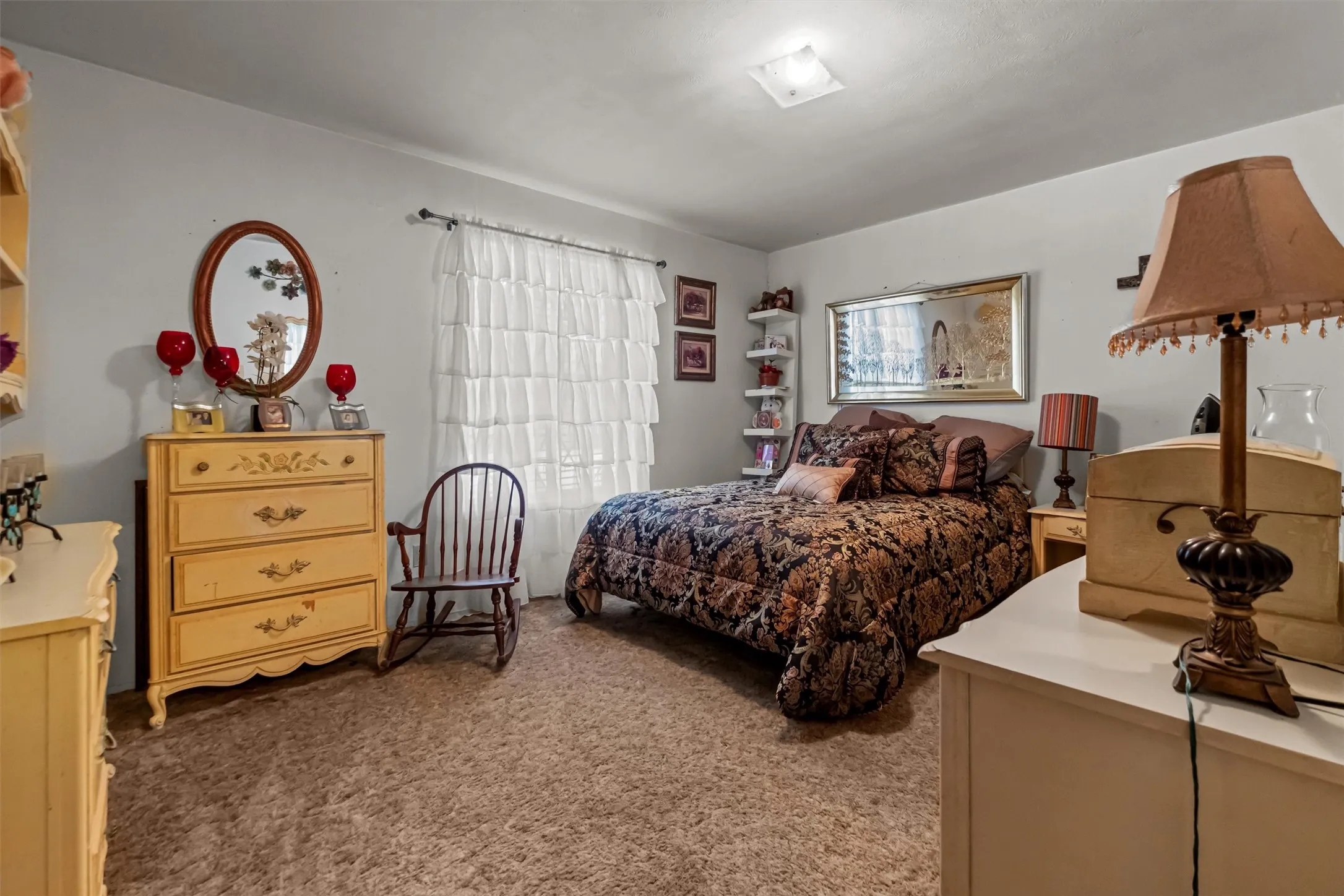 Bedroom featuring light gray walls, carpeted flooring, a window with white layered curtains, and a ceiling-mounted light fixture
