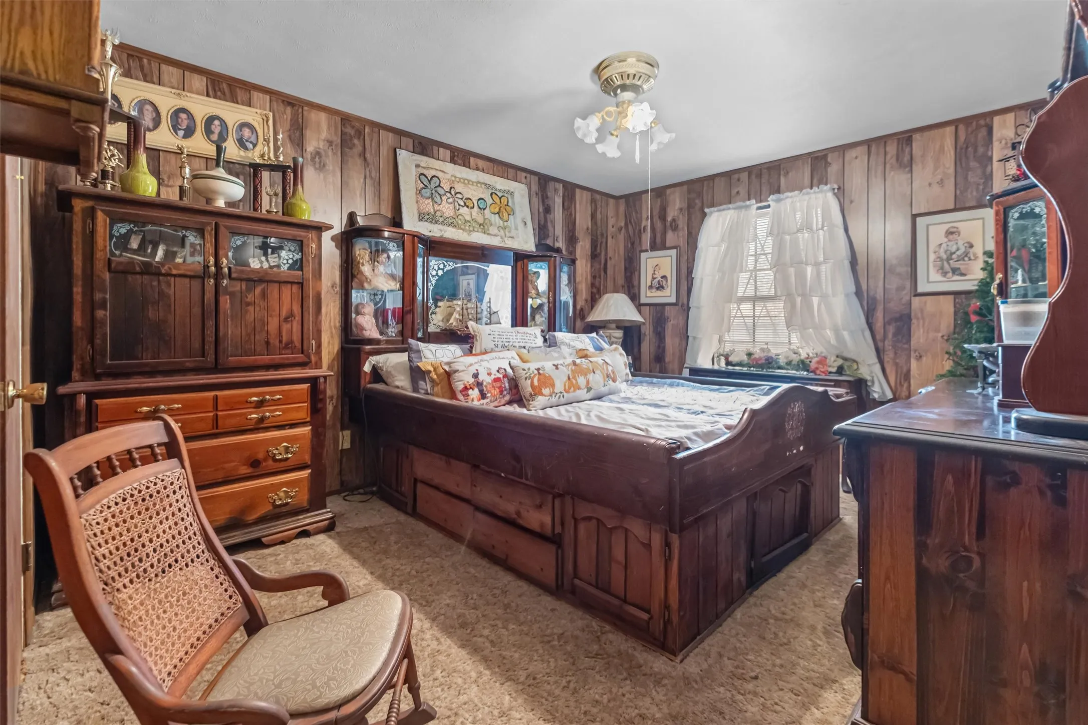 Wood-paneled walls frame this room featuring a window with white curtains, a ceiling-mounted light fixture, and textured carpeting