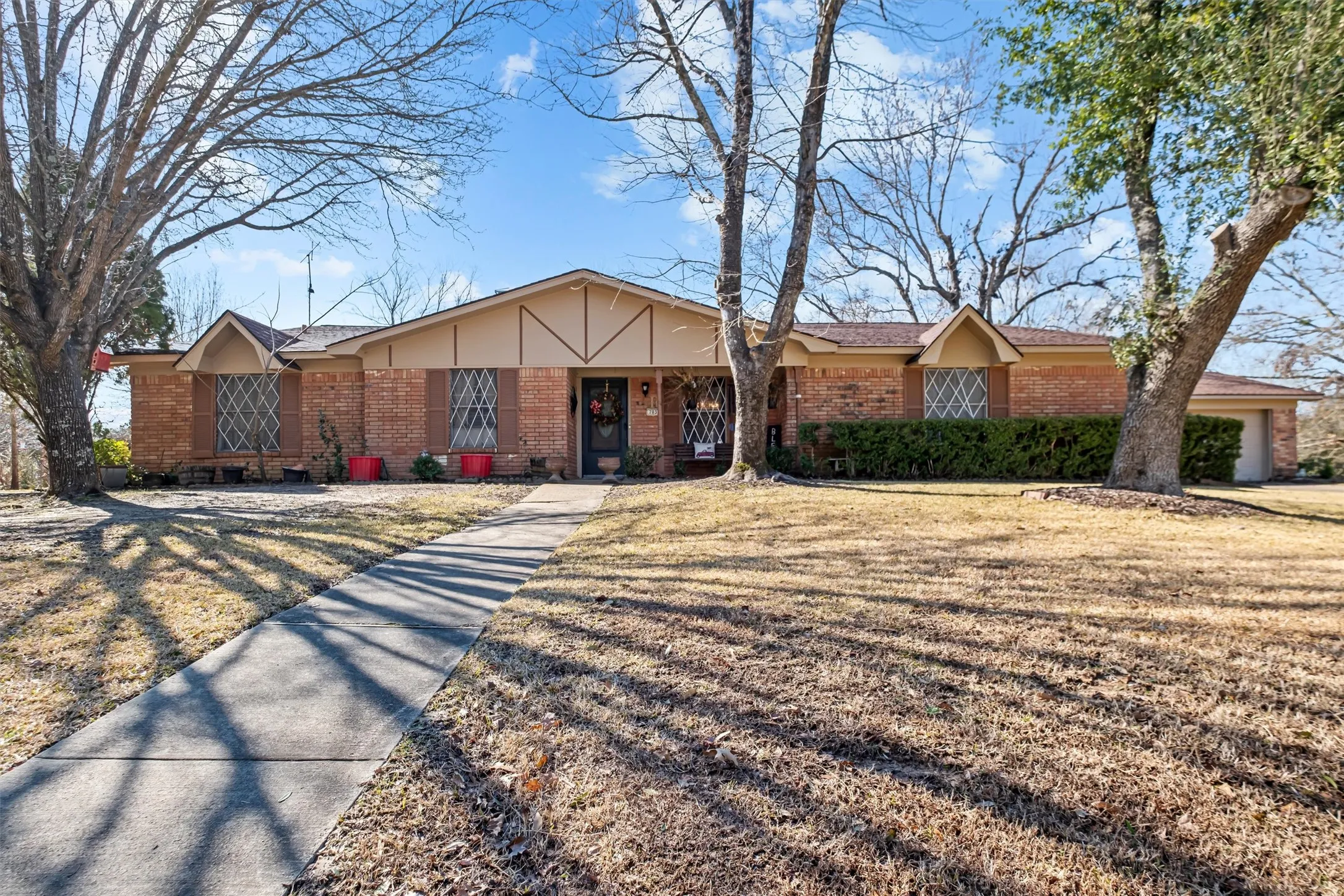 Brick exterior featuring decorative diamond-pattern window grilles, a prominent front walkway, a single-car garage, and mature trees framing the property