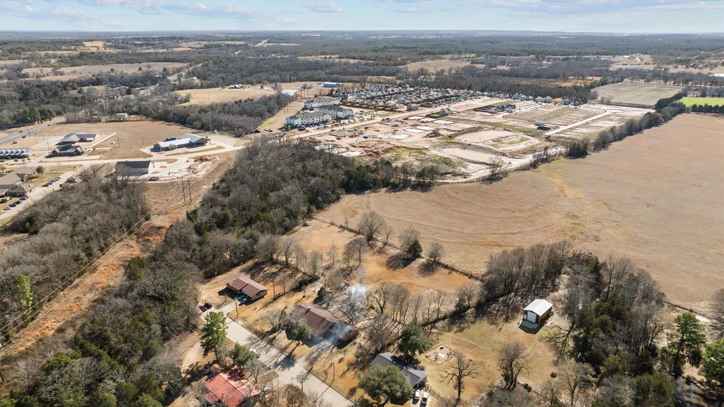 Expansive aerial perspective showcasing diverse terrain including wooded areas, open fields, and residential developments