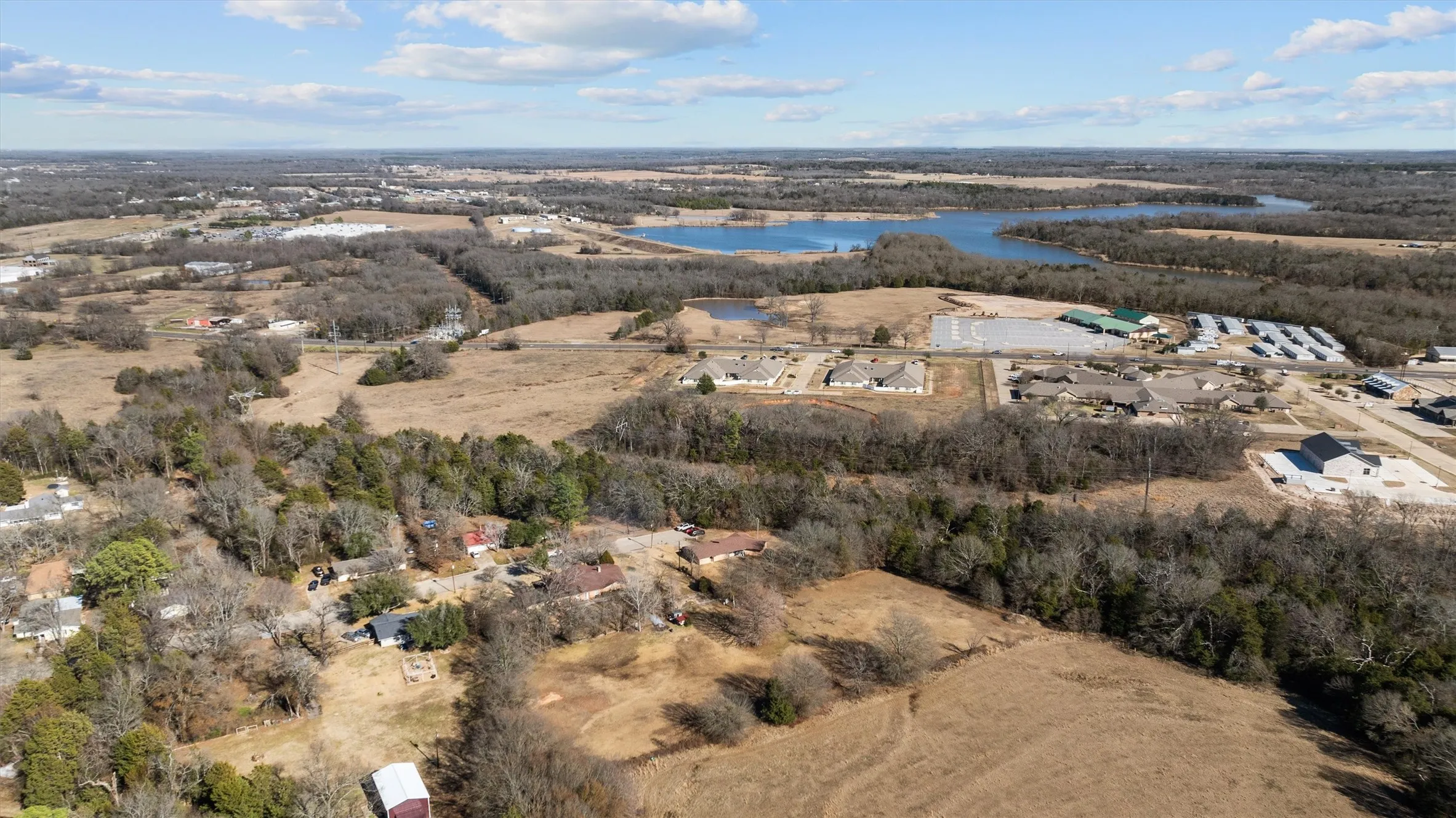 Expansive aerial landscape featuring a large body of water, residential structures, commercial buildings, and undeveloped land