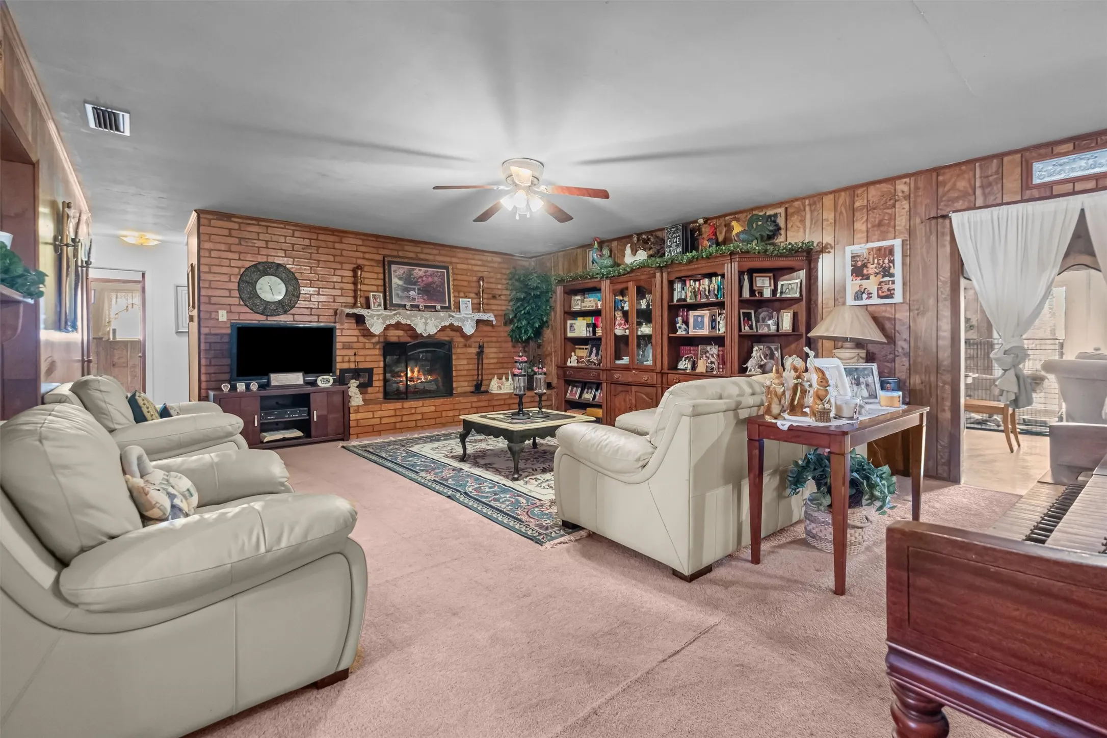 Living area featuring a brick fireplace with a carved mantel, wood paneling, and a ceiling fan