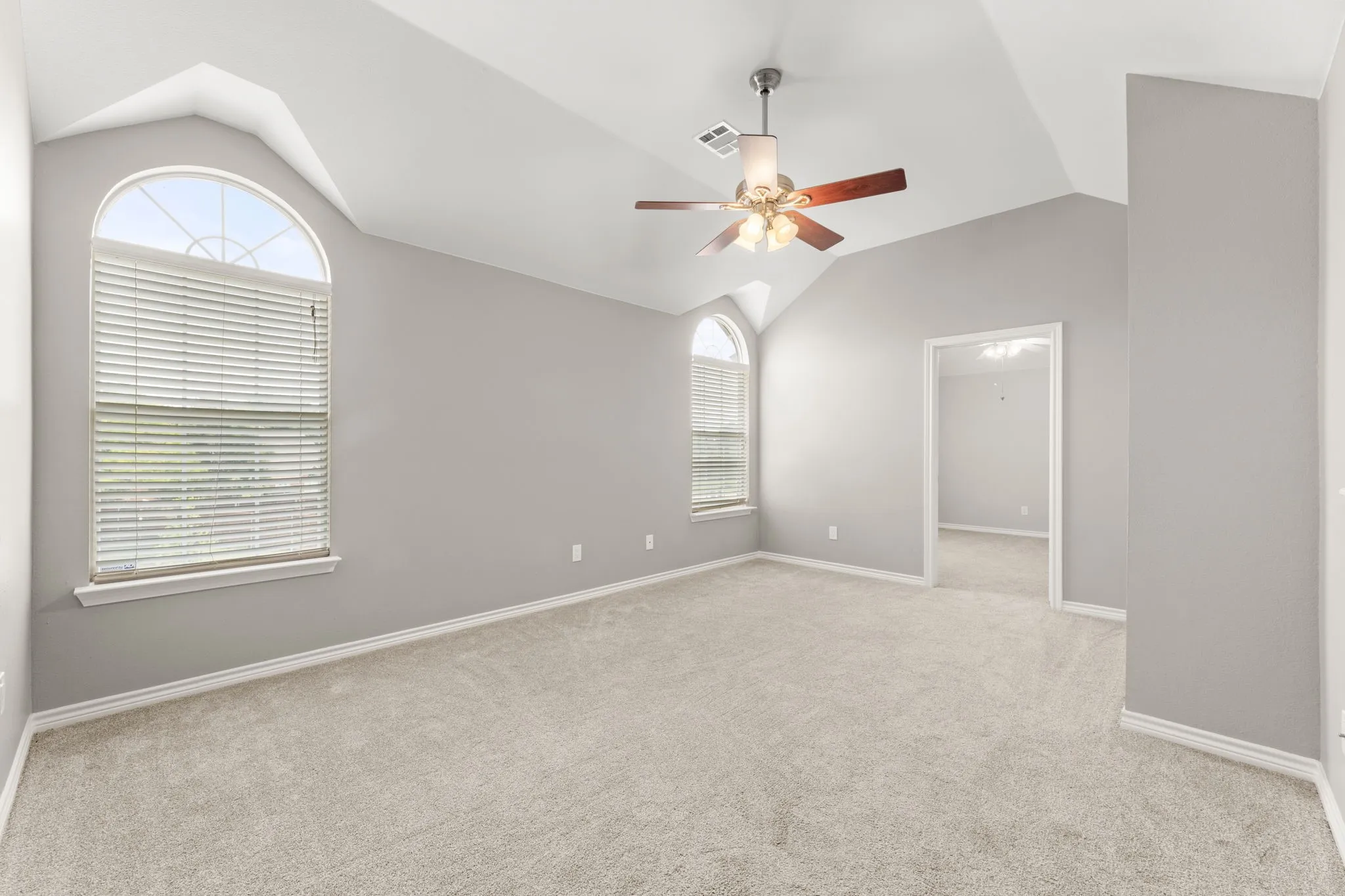 Spacious room featuring vaulted ceilings, light gray wall tones, and plush carpet flooring