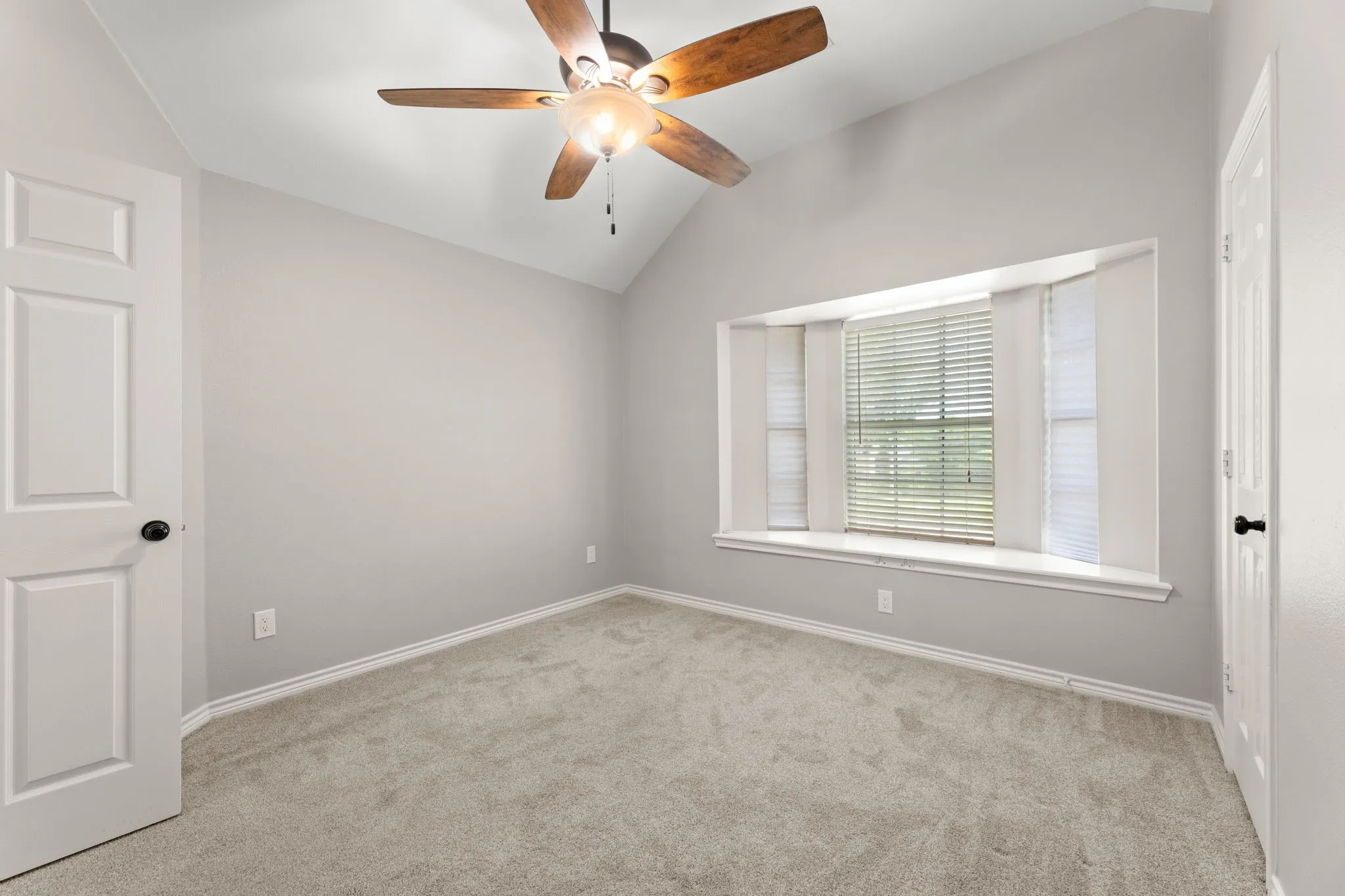Room featuring a bay window with integrated blinds, vaulted ceiling, and a ceiling fan with light fixture