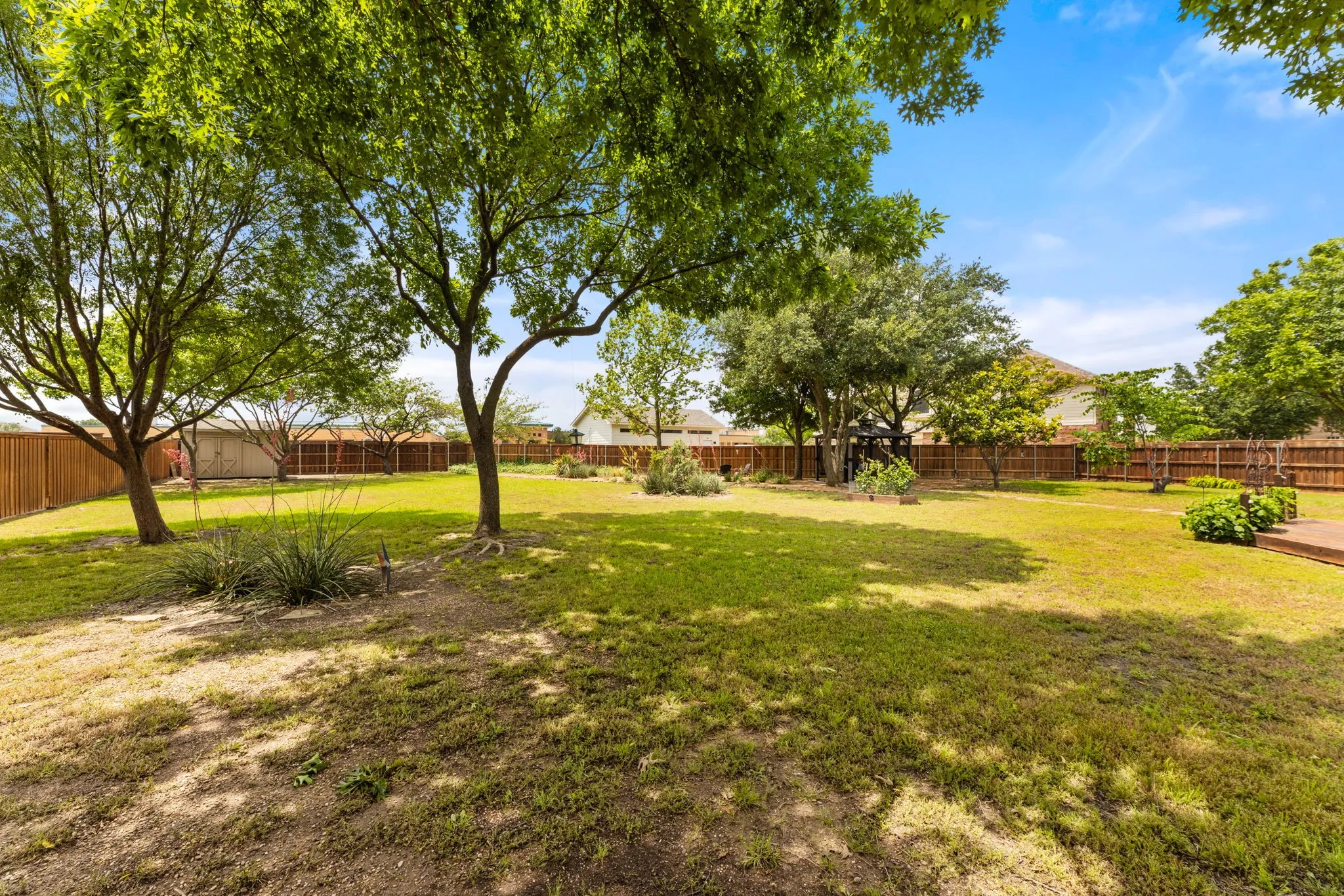 Expansive backyard featuring mature trees, a privacy fence, a wooden deck, and landscaping beds