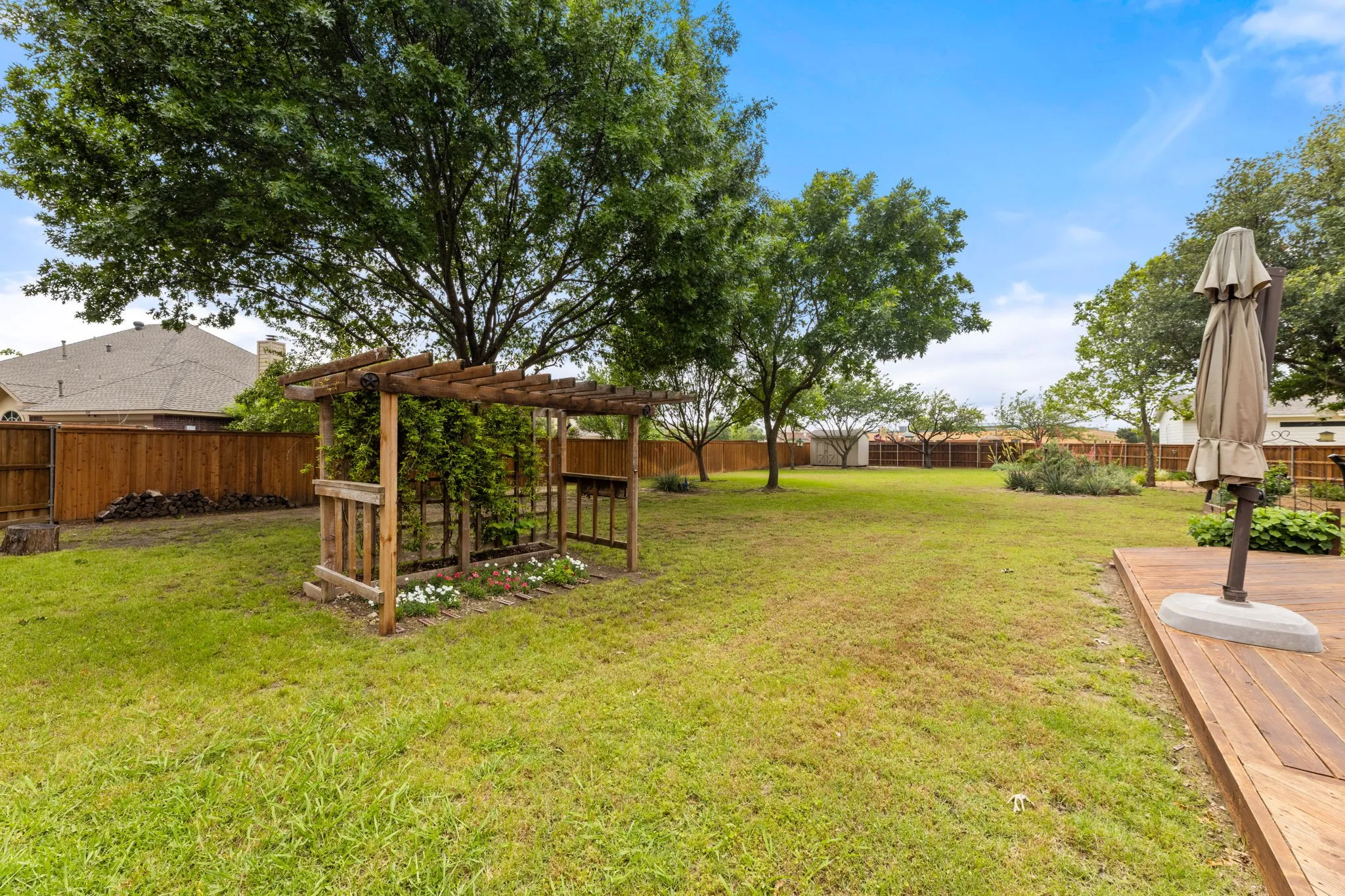 Expansive backyard featuring a large wood-finish deck, mature trees, a wooden pergola structure, and full perimeter fencing