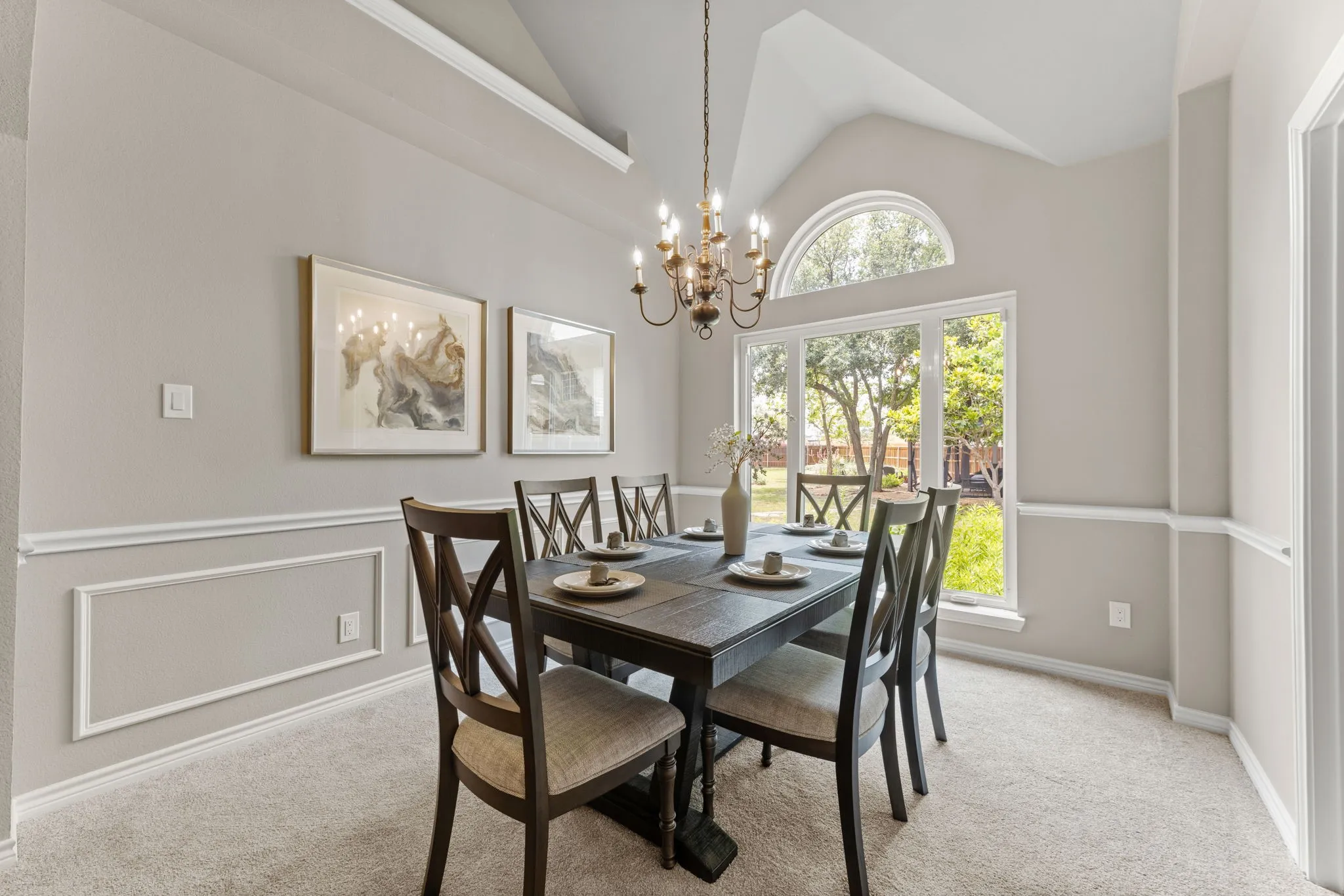 Vaulted ceiling dining area featuring a prominent arched window, chandelier lighting, wainscoting, and carpet flooring