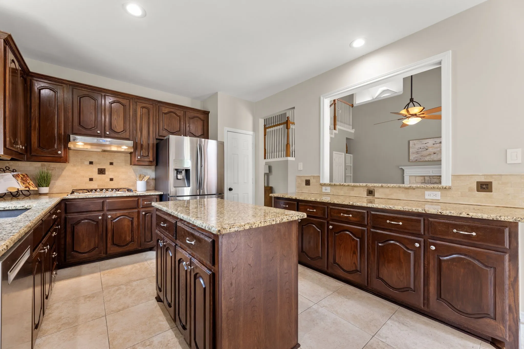 Kitchen featuring rich wood cabinetry, granite countertops, tile flooring, stainless steel appliances, and a pass-through window