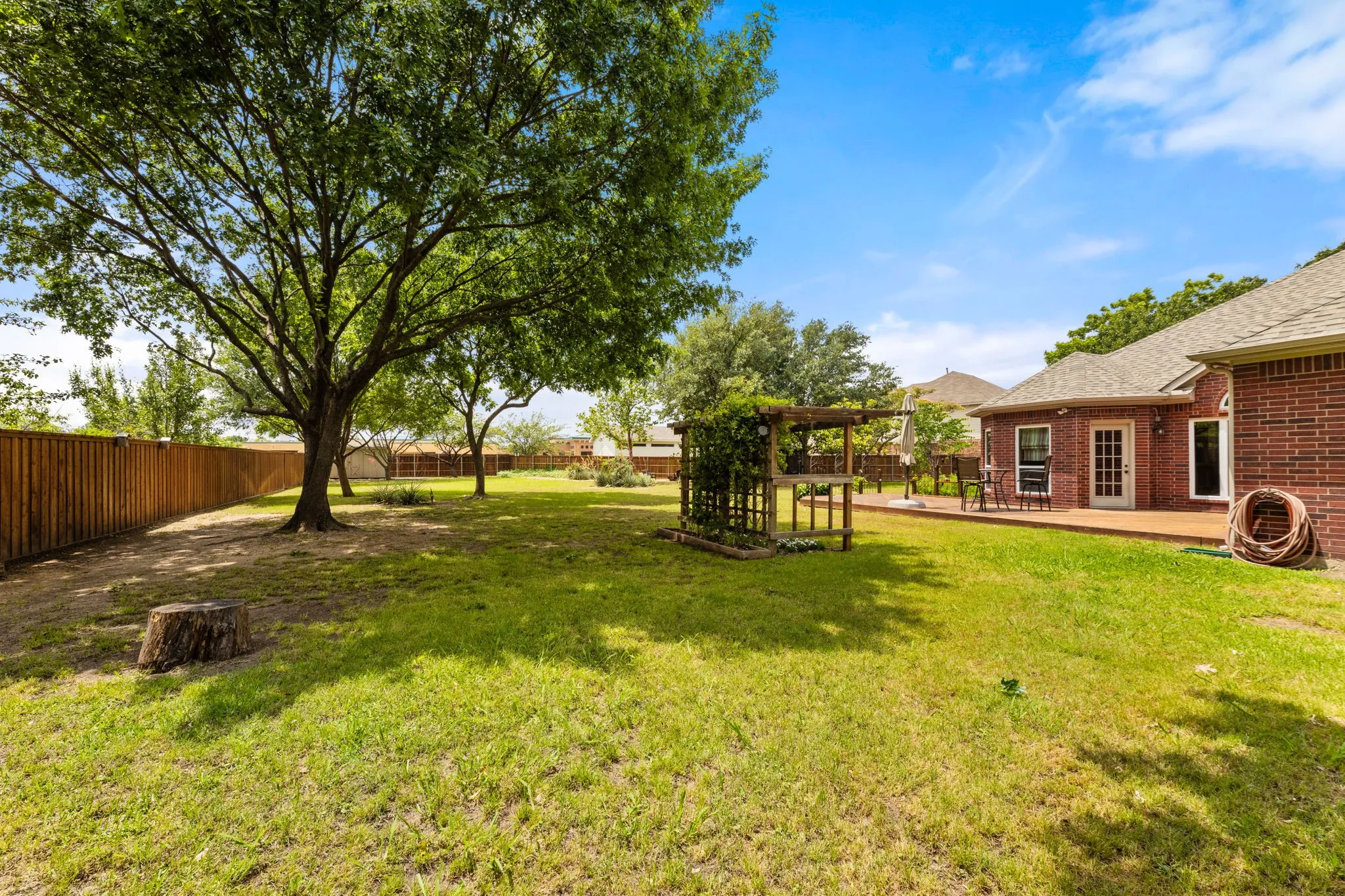 Expansive backyard featuring a manicured lawn, mature shade trees, and a durable wood privacy fence