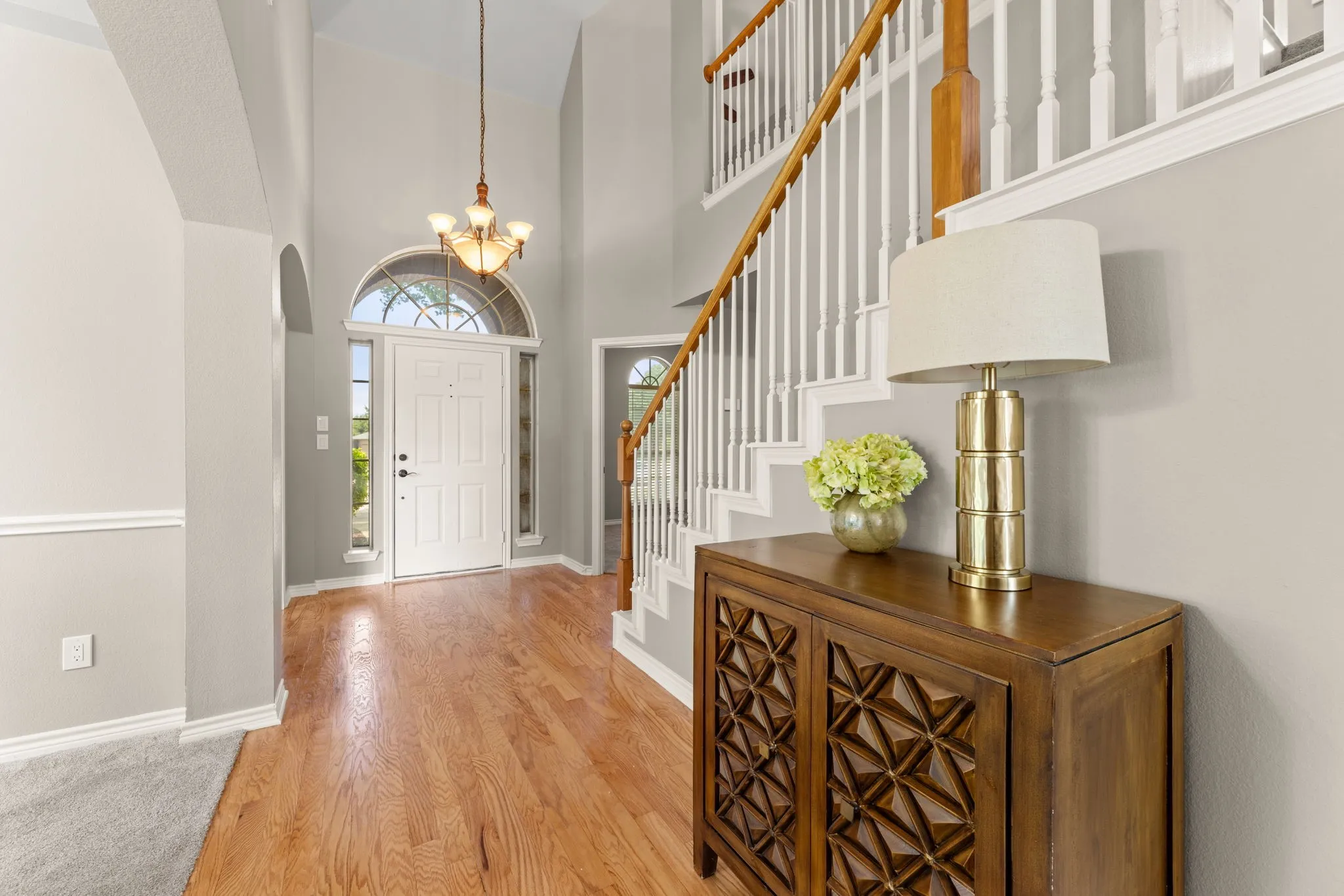 Two-story foyer featuring wood-finish flooring, a grand staircase with white spindles and wood handrail, an arched doorway, and a chandelier