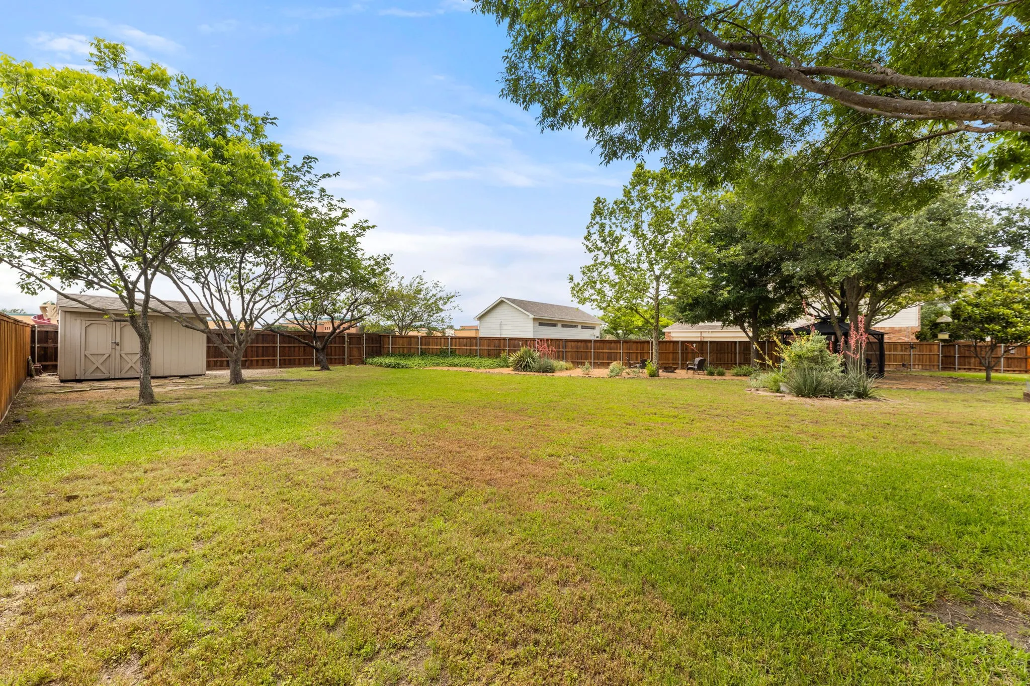 Spacious backyard featuring a storage shed, mature trees, wood fence perimeter, and established landscaping
