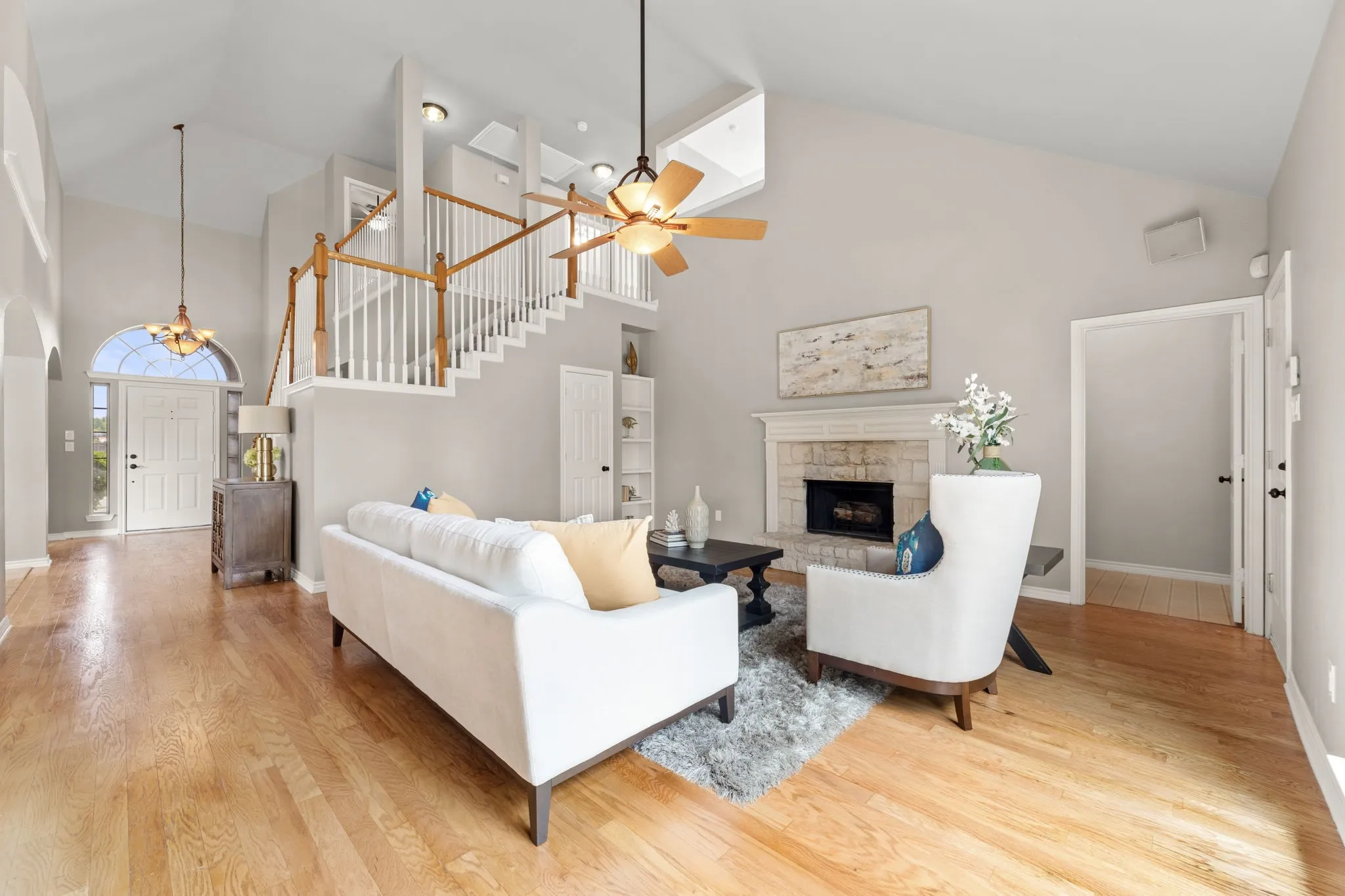 Vaulted ceiling living area featuring wood-finish flooring, a stone-surround fireplace with a white mantel, and a multi-level staircase with white balusters and wood handrails