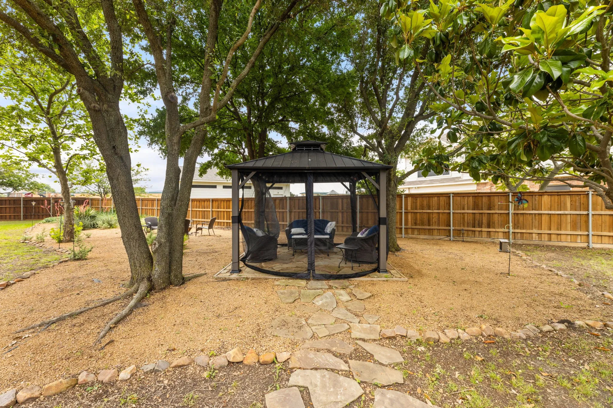 Backyard featuring a covered gazebo with screening, mature trees, a stone pathway, and a wood privacy fence