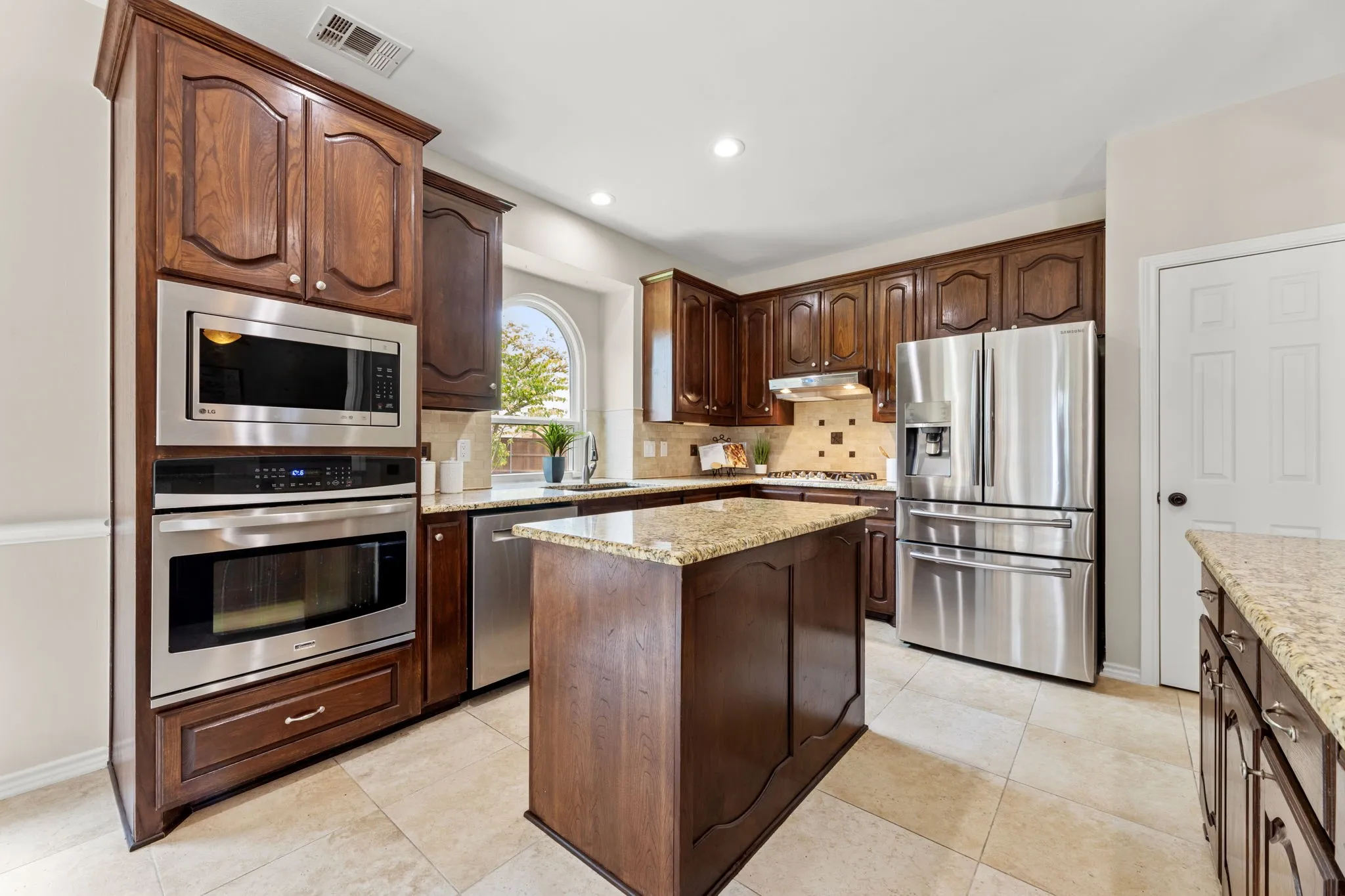 Kitchen featuring a built-in oven and microwave, stainless steel appliances, dark wood cabinetry, a granite island, and tiled flooring