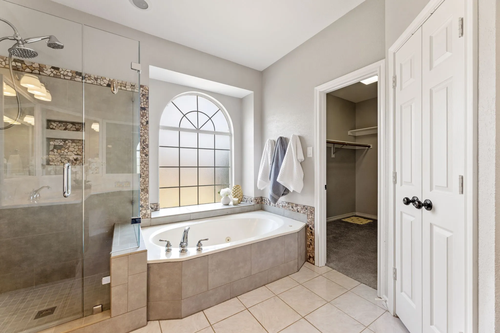 Soaking tub with an arched window, paired with a glass-enclosed shower featuring a mosaic tile accent