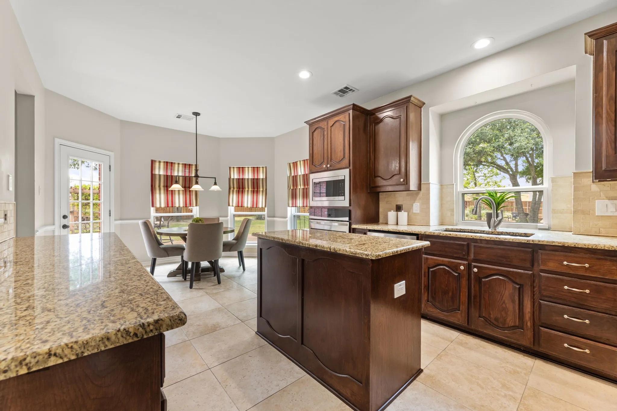 Kitchen featuring an arched window, wood cabinetry, built-in microwave and oven, a center island, and granite countertops