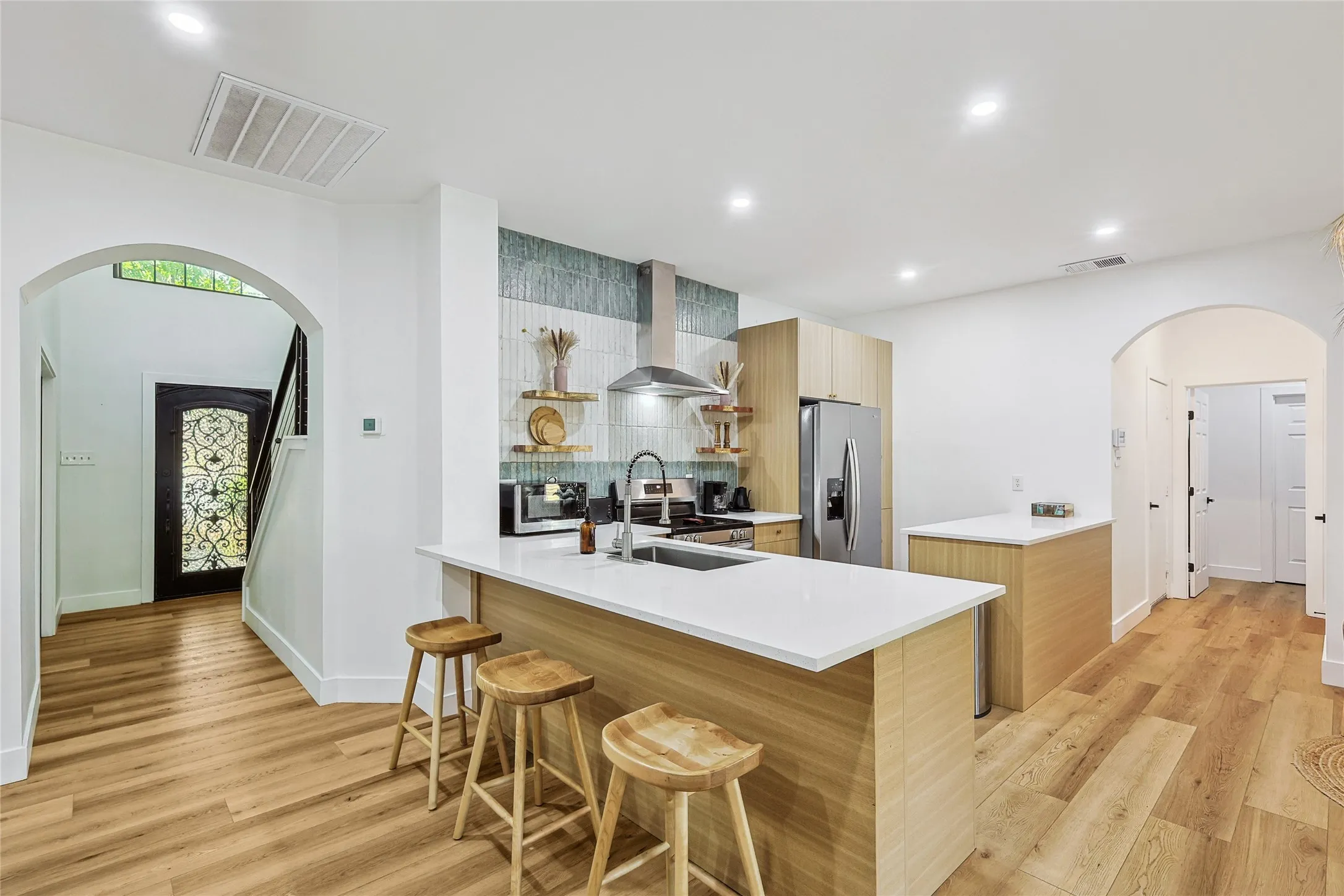 Kitchen featuring a sink, arched walkways, visible vents, wall chimney range hood, and appliances with stainless steel finishes