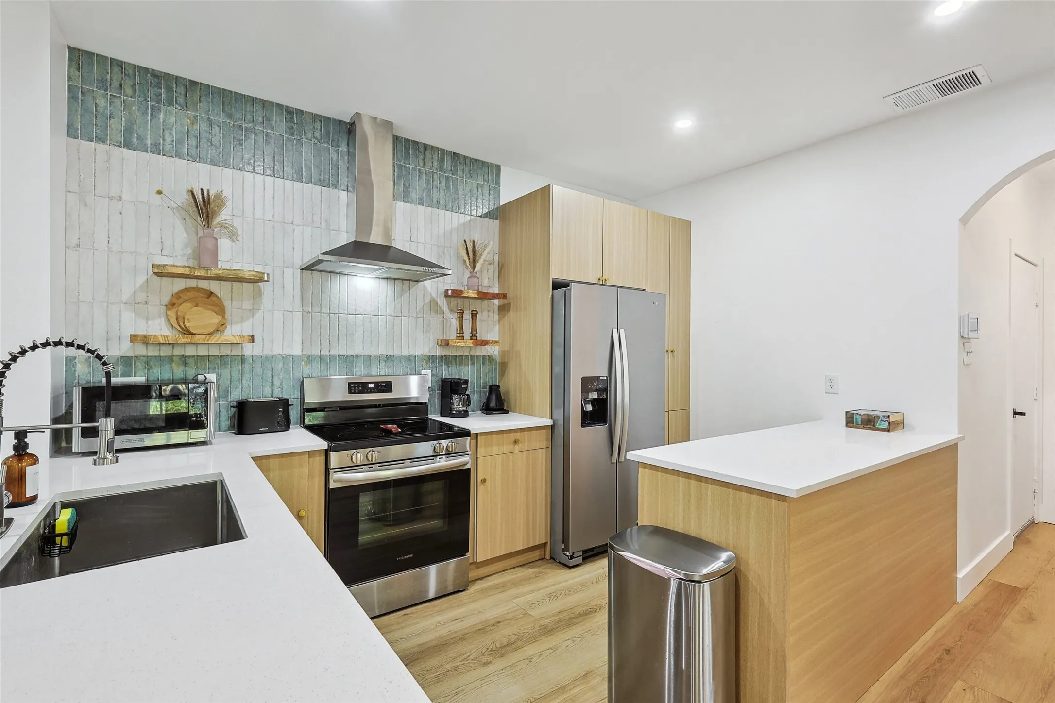 Kitchen with open shelves, a sink, visible vents, wall chimney range hood, and appliances with stainless steel finishes
