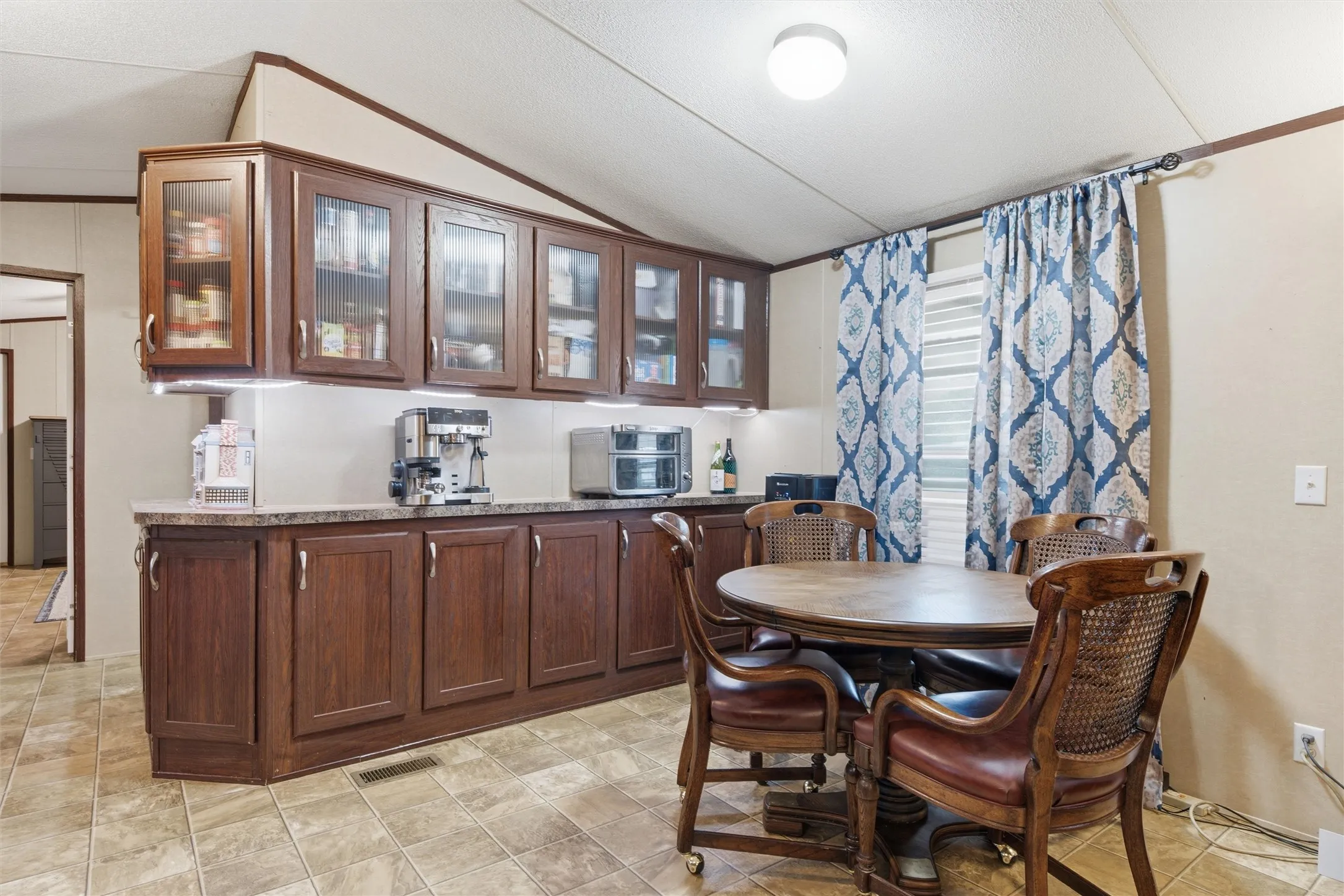 Kitchen area featuring wood-finish cabinetry with glass-front upper cabinets, a light-toned countertop, and tiled flooring