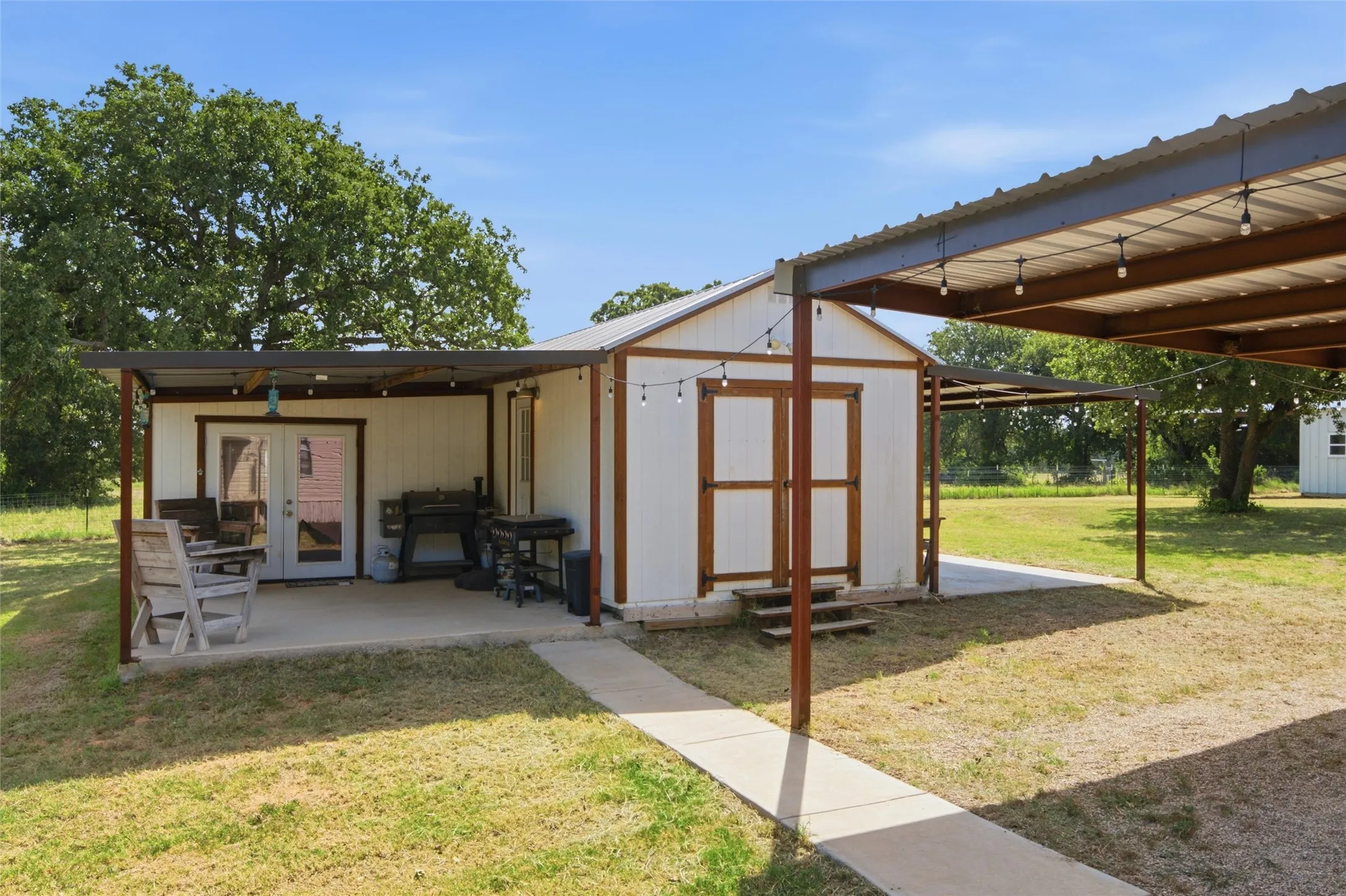 White outbuilding featuring a covered concrete patio, French doors, and double storage doors