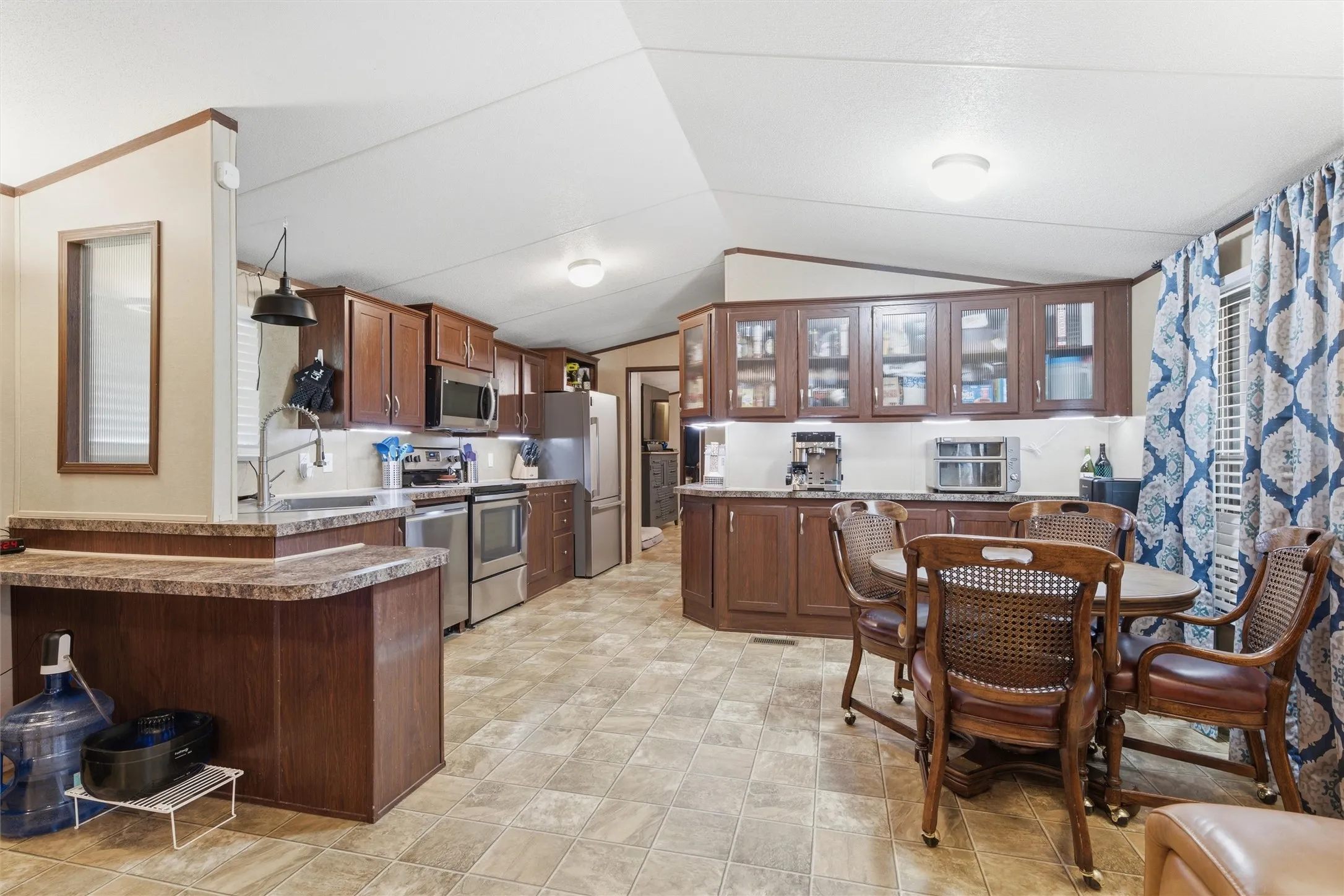 Kitchen featuring wood-finish cabinetry, stainless steel appliances, stone-look countertops, and tile-look flooring