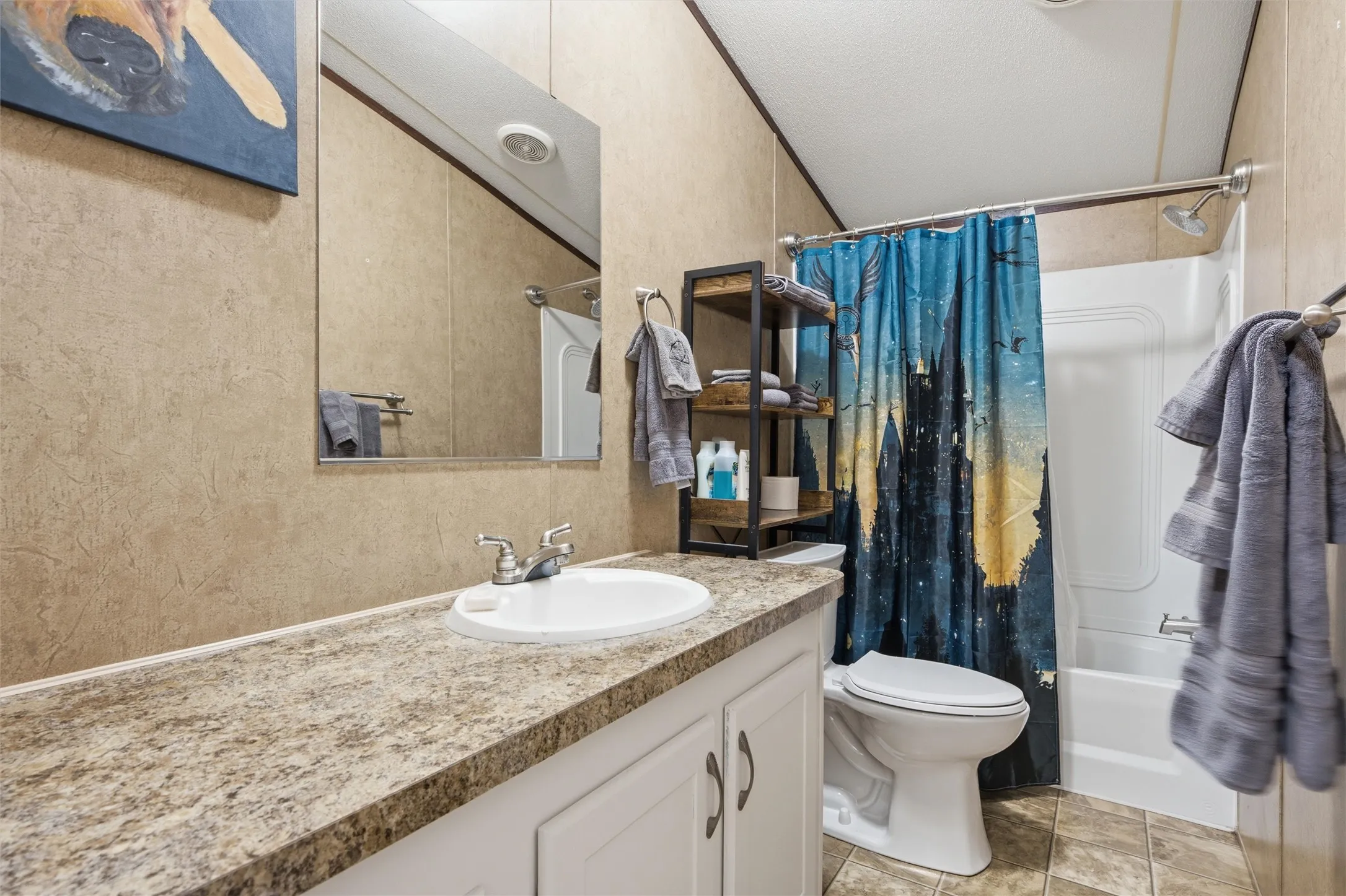Bathroom featuring a vanity with a white basin and a stone-look countertop, a built-in tub with shower, and tile-look flooring