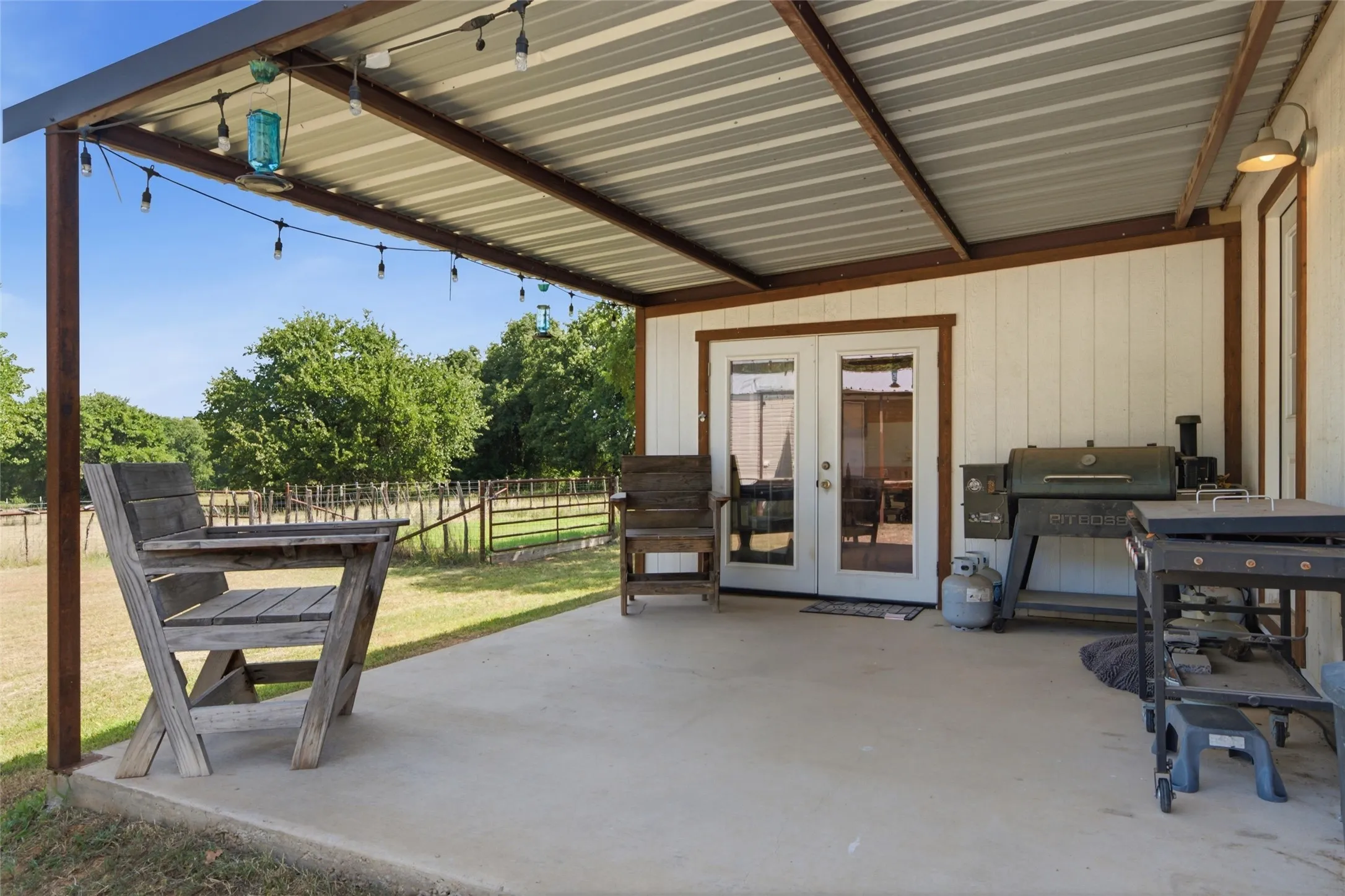 Expansive covered patio featuring a corrugated metal roof, string lighting, and direct access through double glass panel doors