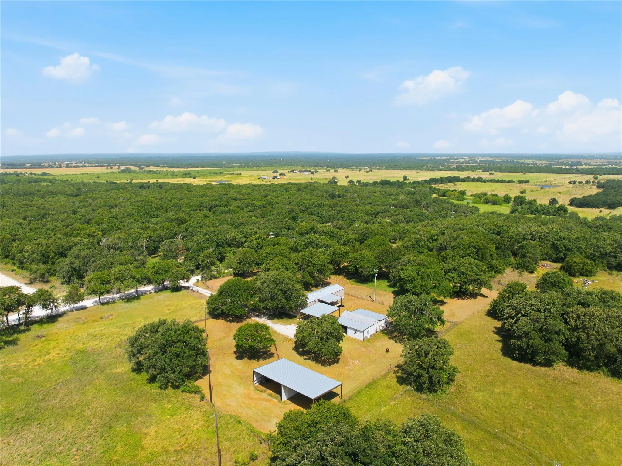 Expansive acreage featuring multiple structures, mature trees, open fields, and a clear sky