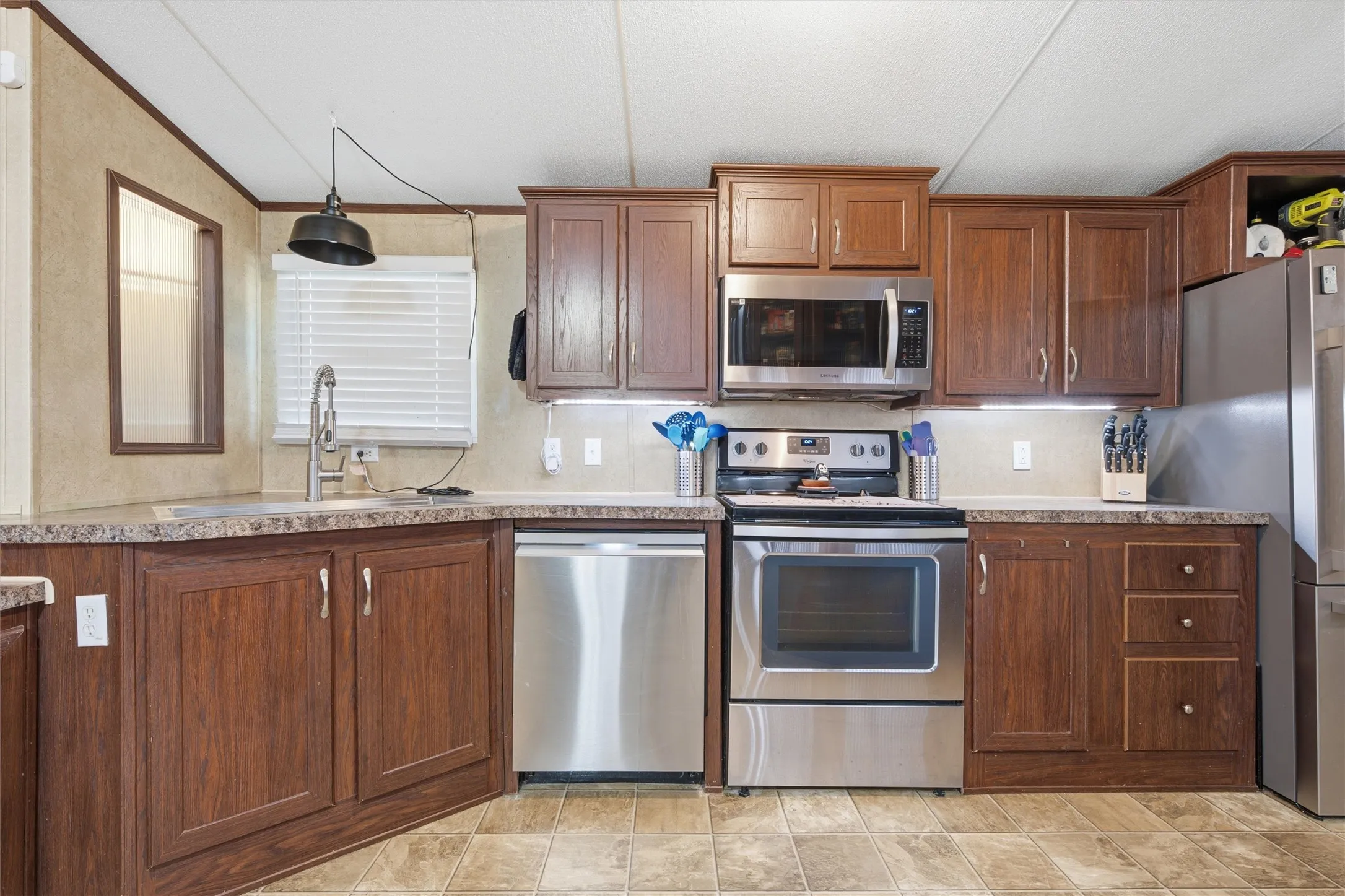Kitchen featuring wood-finish cabinetry, stainless steel appliances, a double basin sink, and ample countertop space