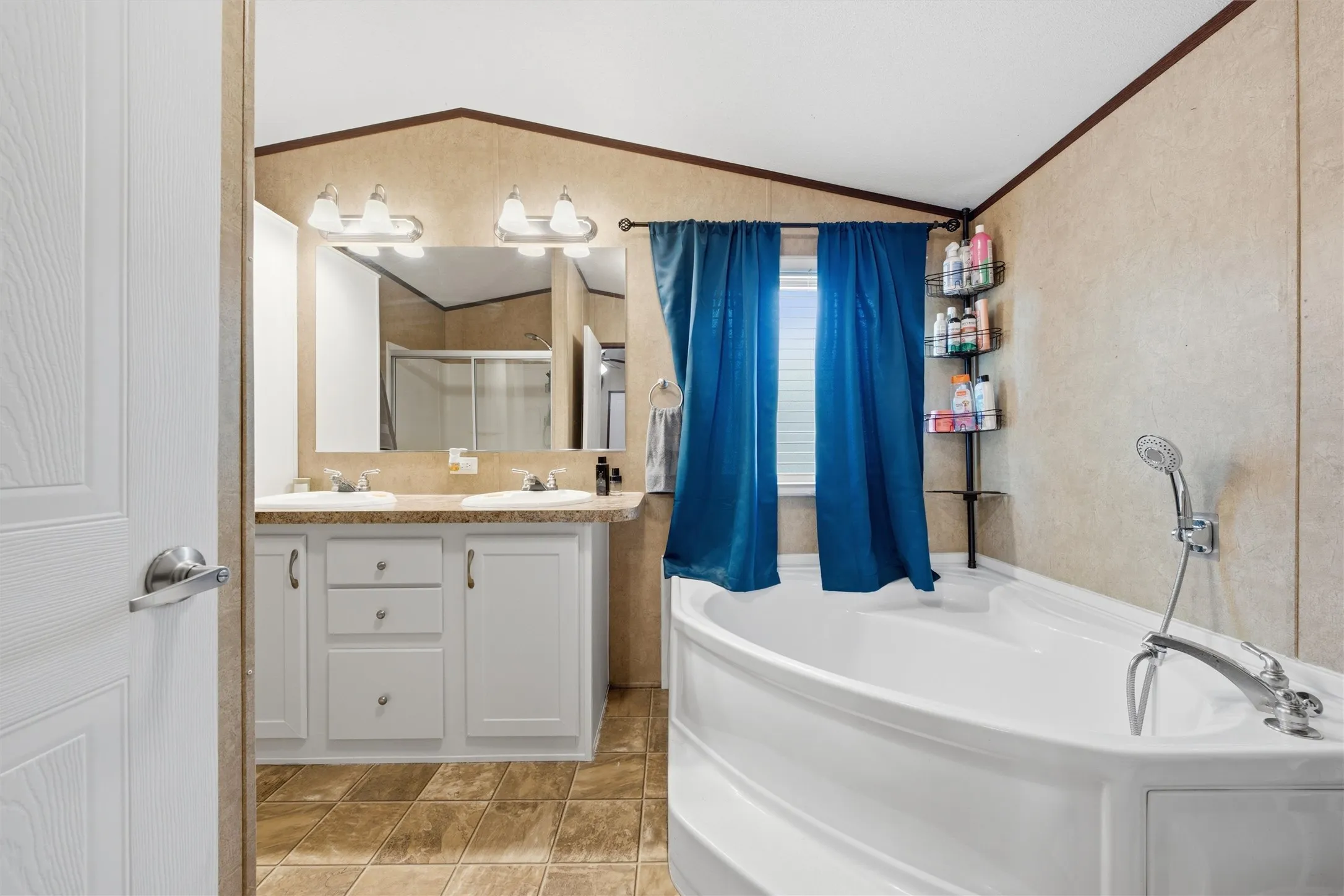 Bathroom featuring a dual vanity with light-toned countertops, two mirrors, and a built-in bathtub with an attached shower sprayer
