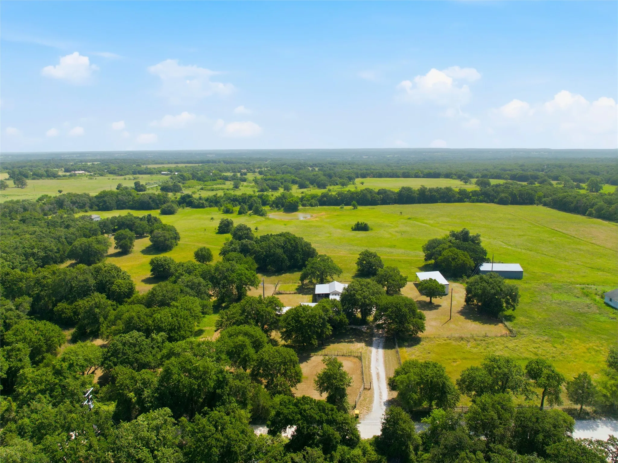 Expansive property featuring mature trees, multiple structures, and vast green fields
