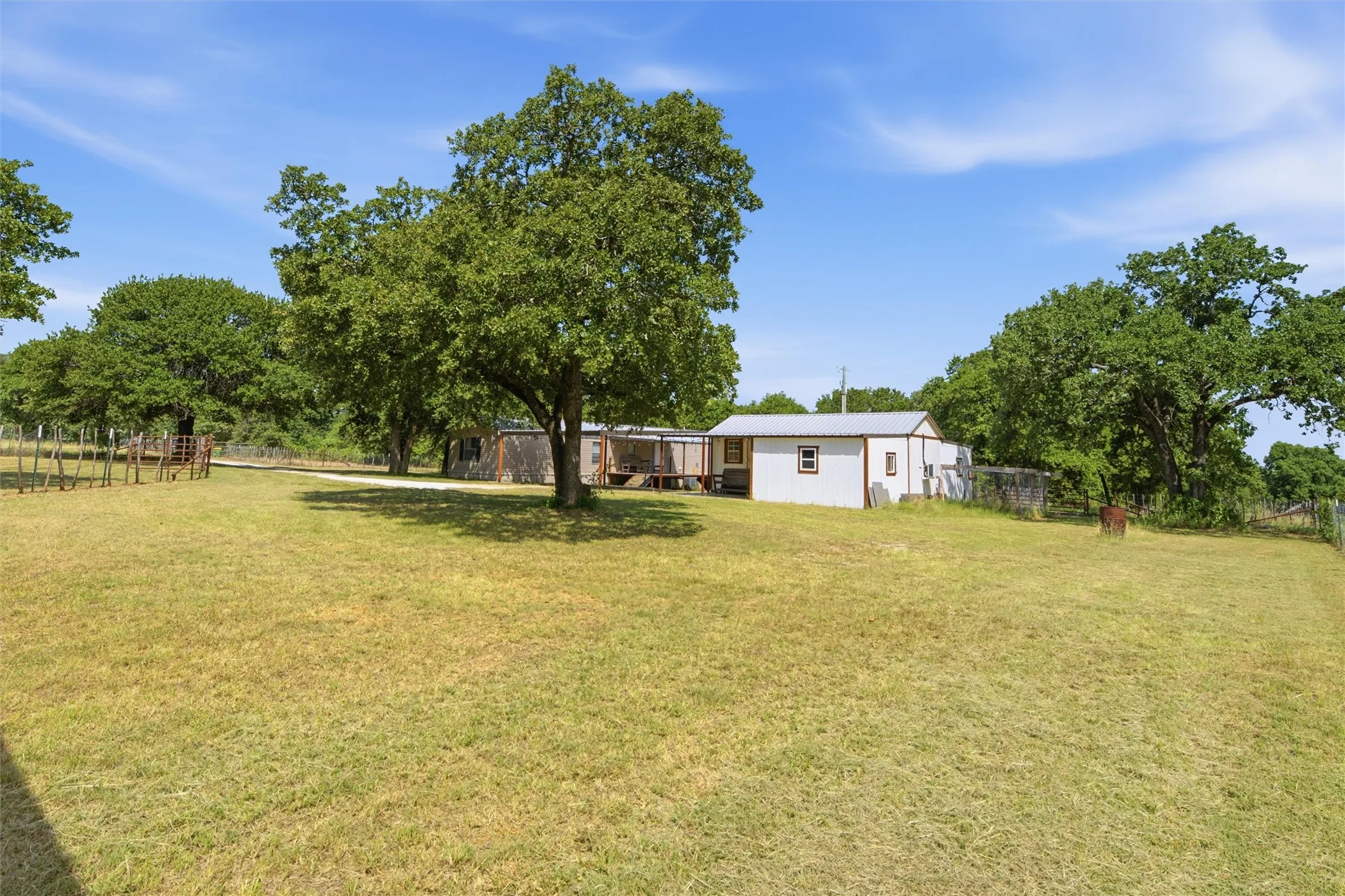 Expansive grassy area featuring mature trees and a white outbuilding with a metal roof