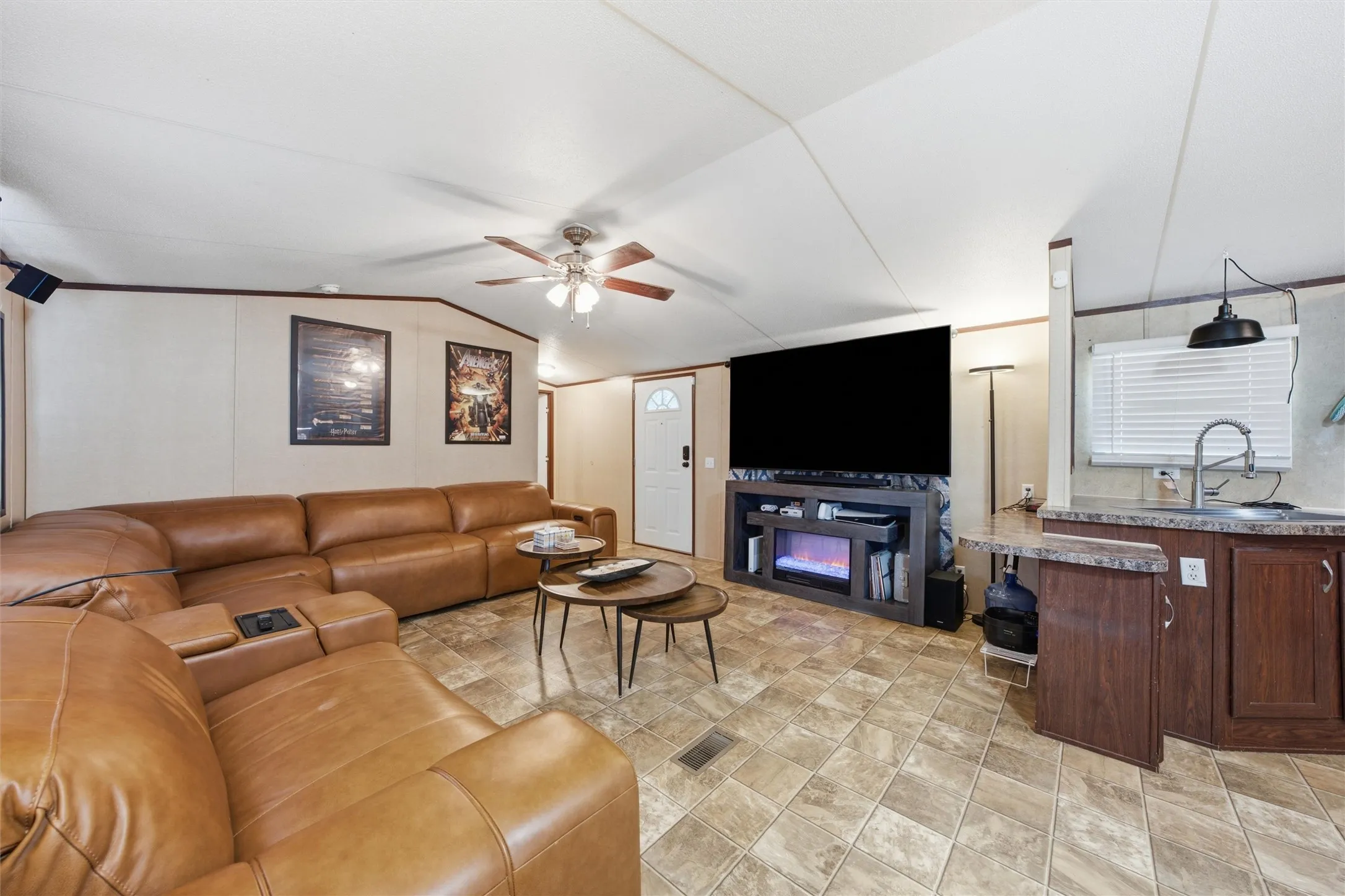Open-concept living area featuring a decorative ceiling fan, patterned tile flooring, and a built-in media console with an electric fireplace