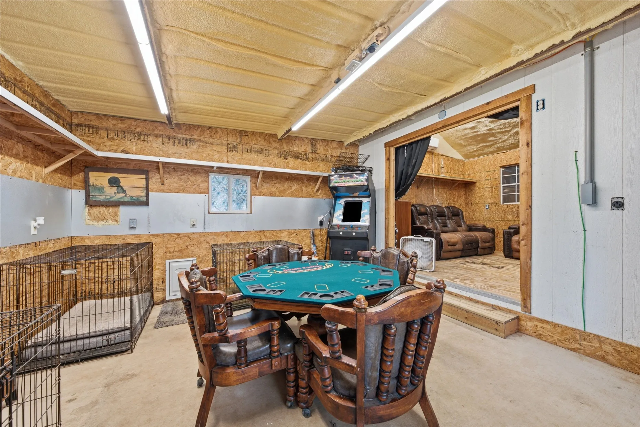 Versatile interior space featuring concrete flooring, exposed plywood walls, and an insulated ceiling with fluorescent lighting