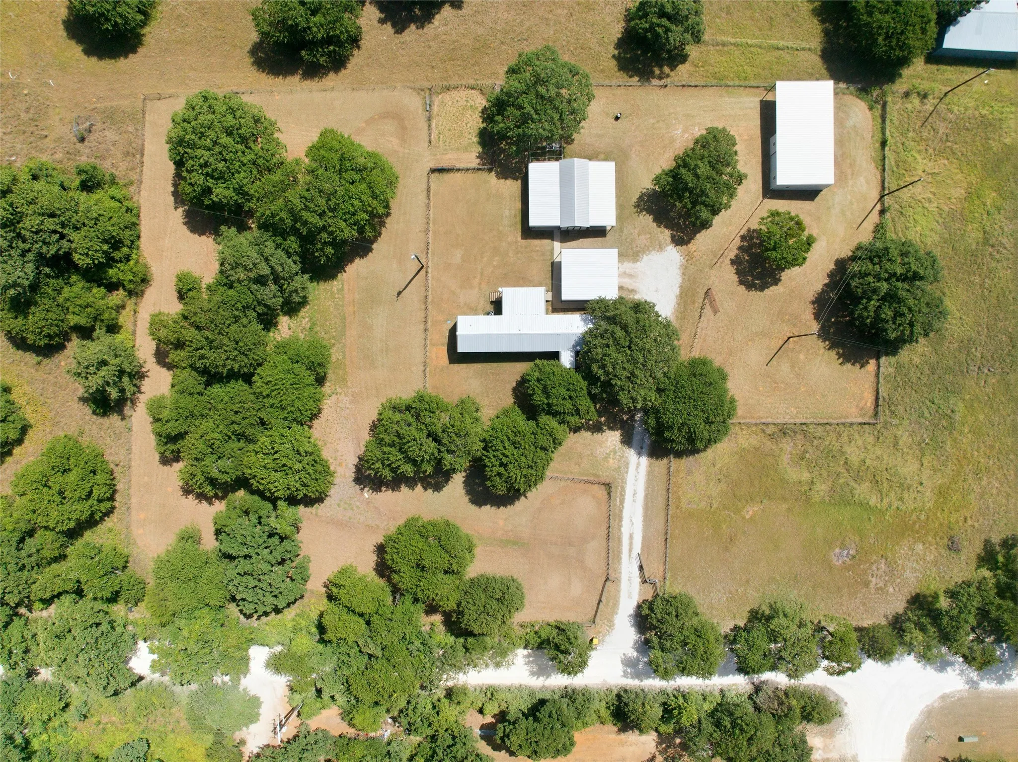 Extensive rural property featuring multiple structures with metal roofs, mature trees, open land, and perimeter fencing
