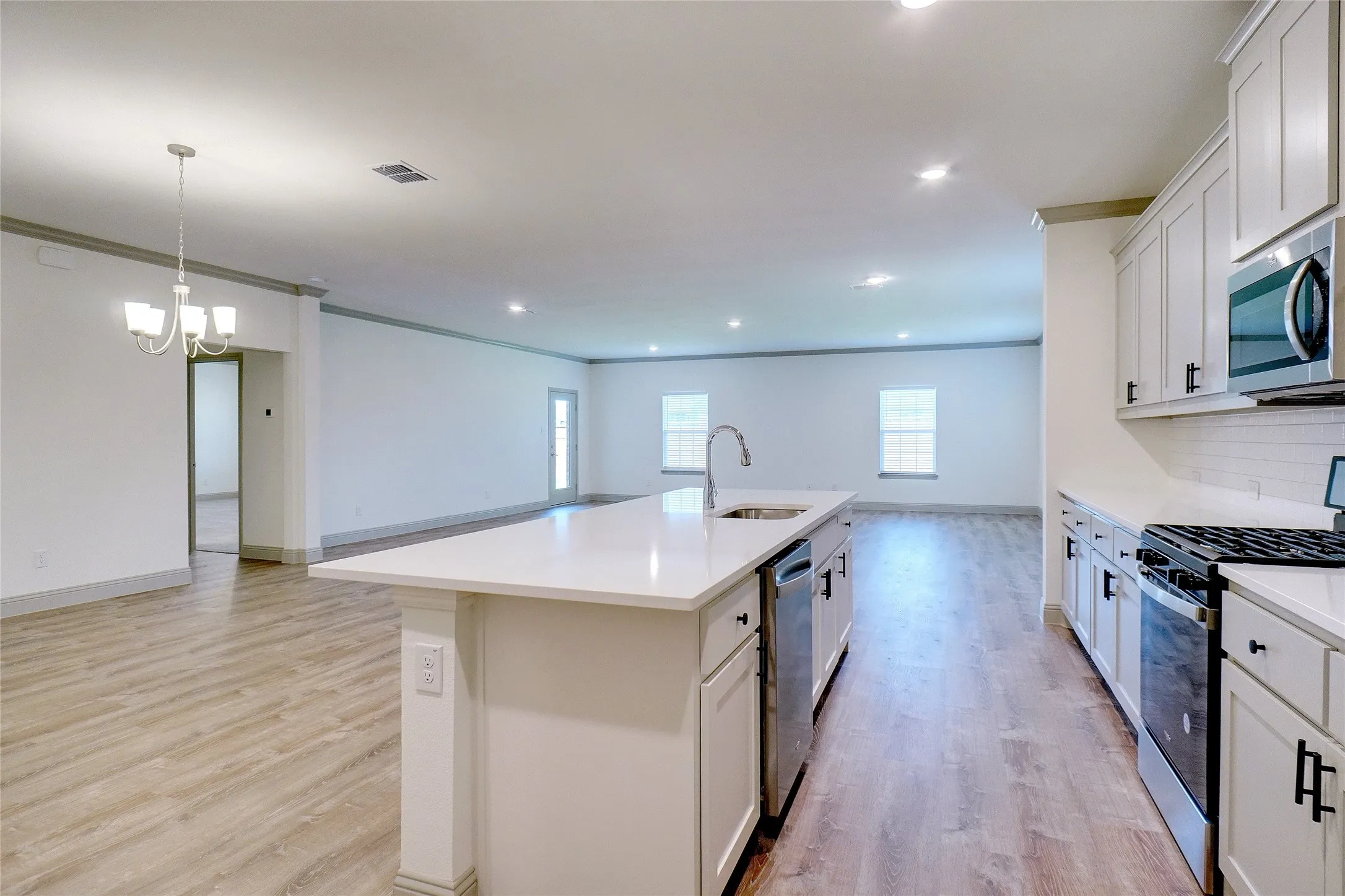 Open-concept kitchen and living area featuring wood-finish flooring, recessed lighting, and a white island with an undermount sink