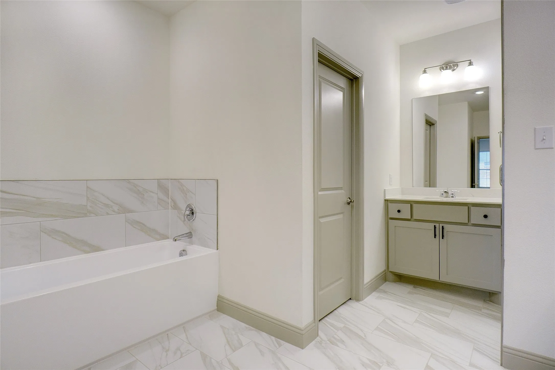 Bathroom featuring a white built-in tub with a tiled surround, a light-toned vanity with a countertop, and a mirror with overhead lighting