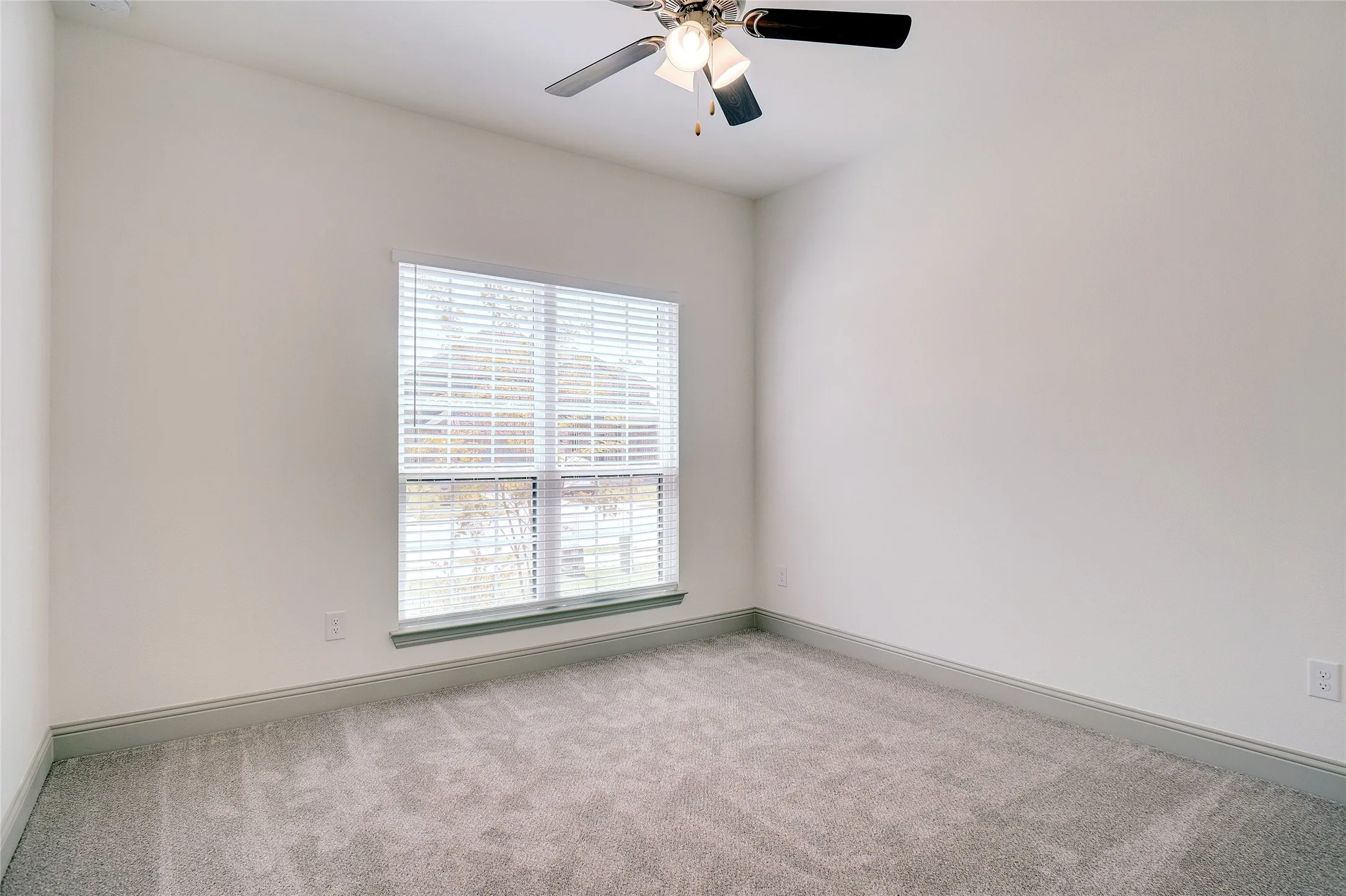 Carpeted room featuring a single window with blinds, a ceiling fan, white walls, and gray baseboards